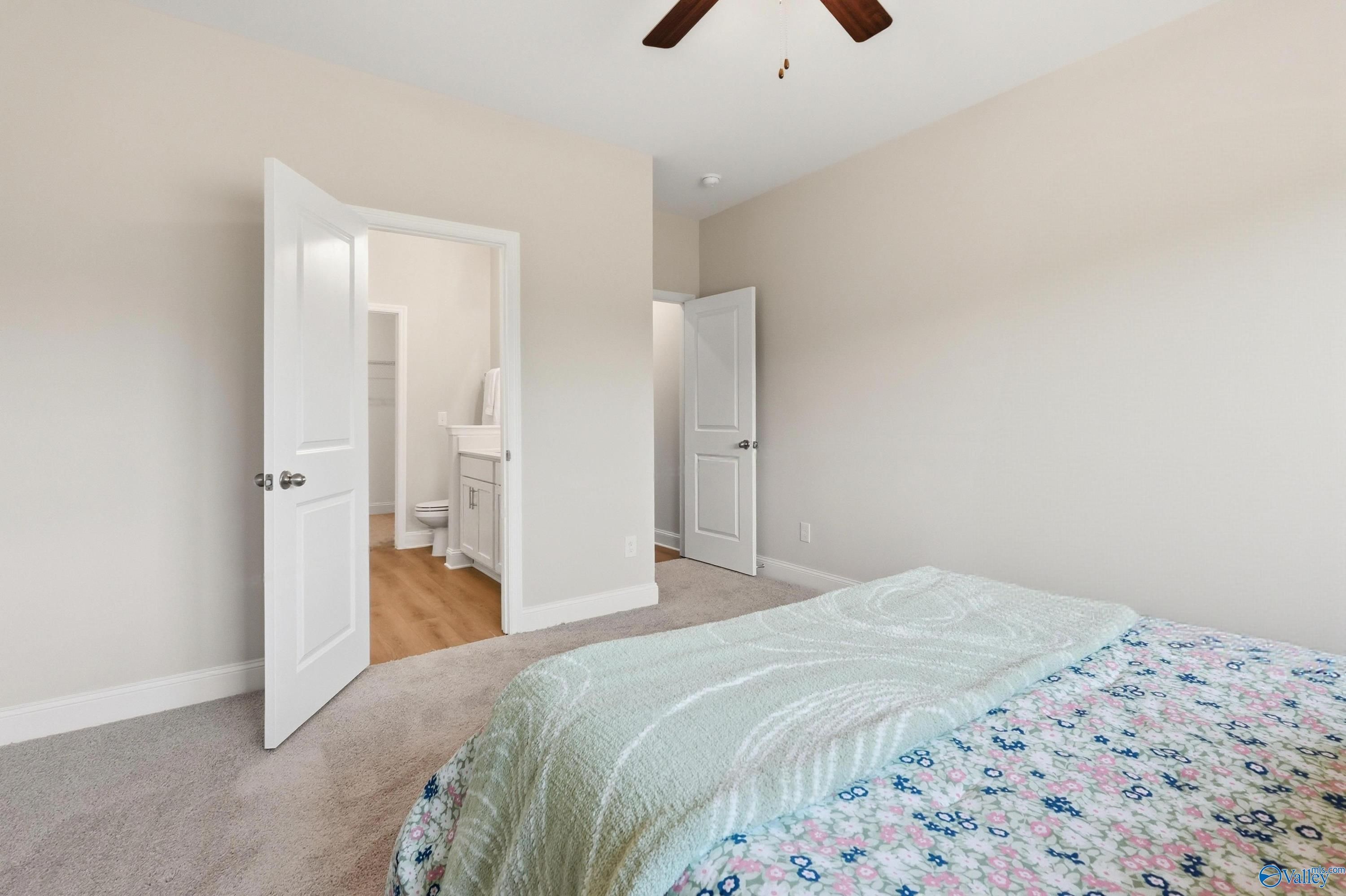 Master bedroom with floral quilt bed, ceiling fan, and open en-suite bath in Davidson Homes The Asheville, Toney AL