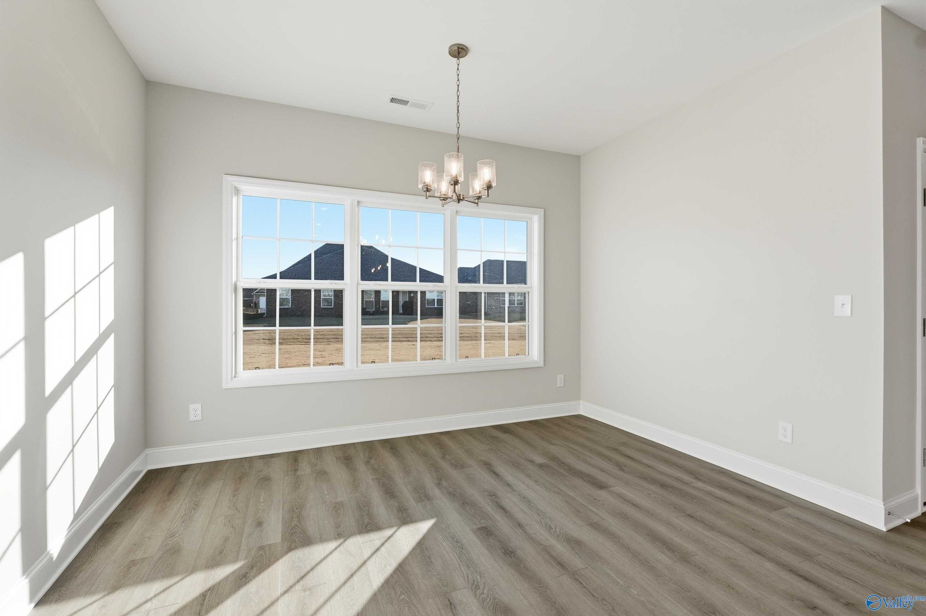 Bright sunlit room with large triple windows, modern chandelier, and hardwood floors in The Montgomery B home, Toney, Alabama