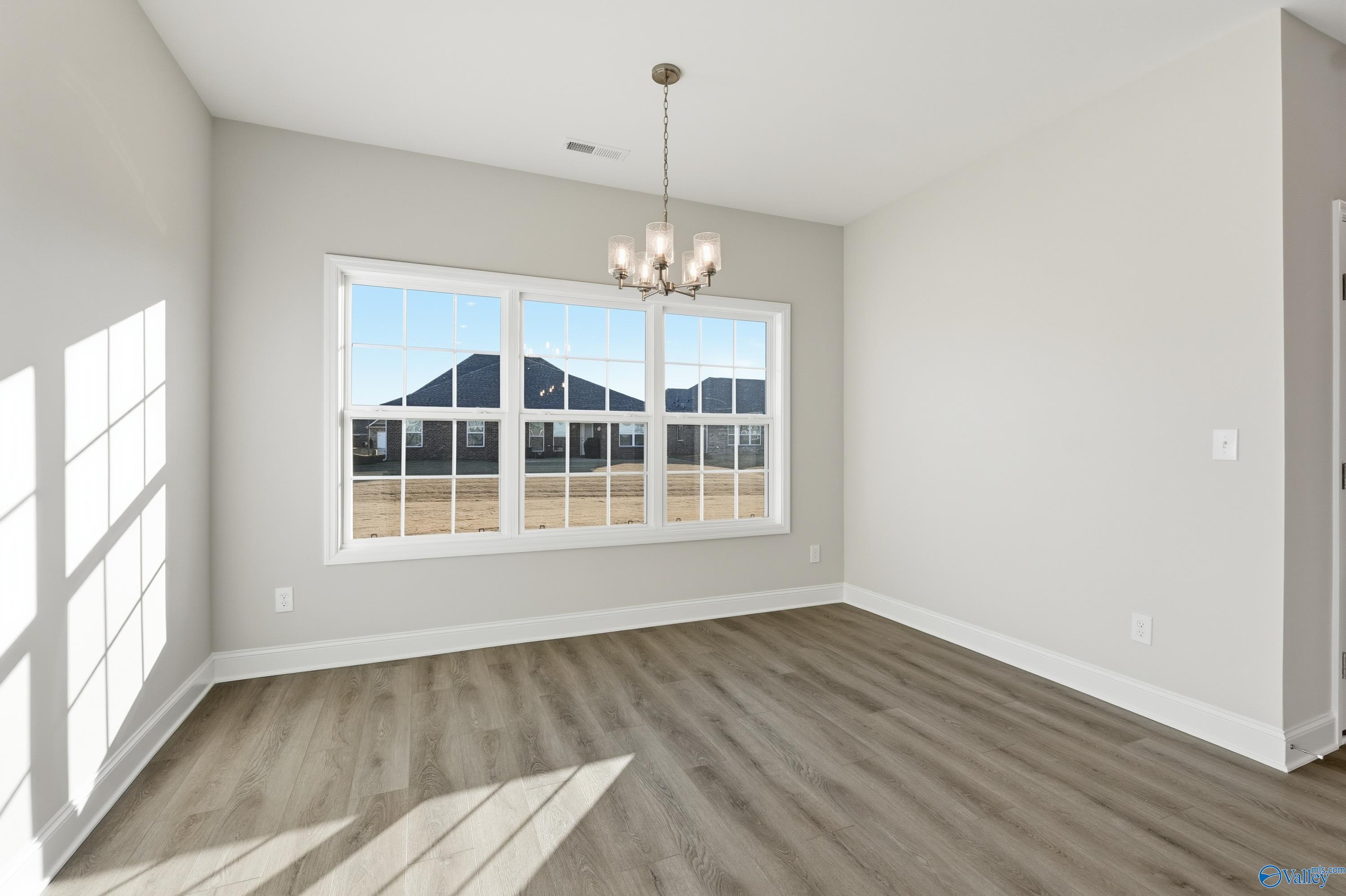 Bright dining room with chandelier, gray walls, hardwood floors, and large windows overlooking homes in The Montgomery B, Toney, Alabama