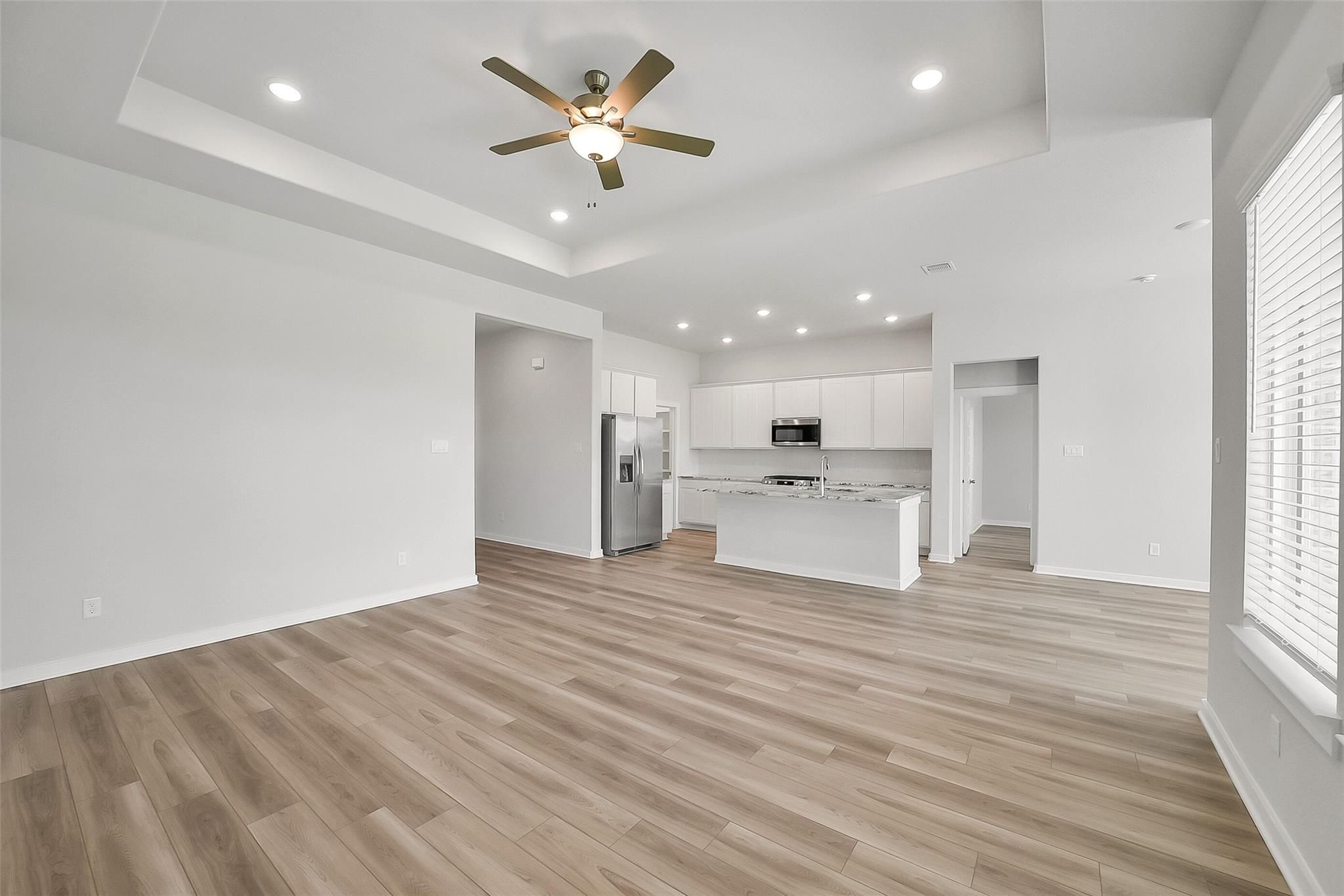 Open-concept kitchen and living room with white cabinets, stainless steel appliances, island, wood flooring, and ceiling fan in Davidson Homes Acadia A, Katy Texas