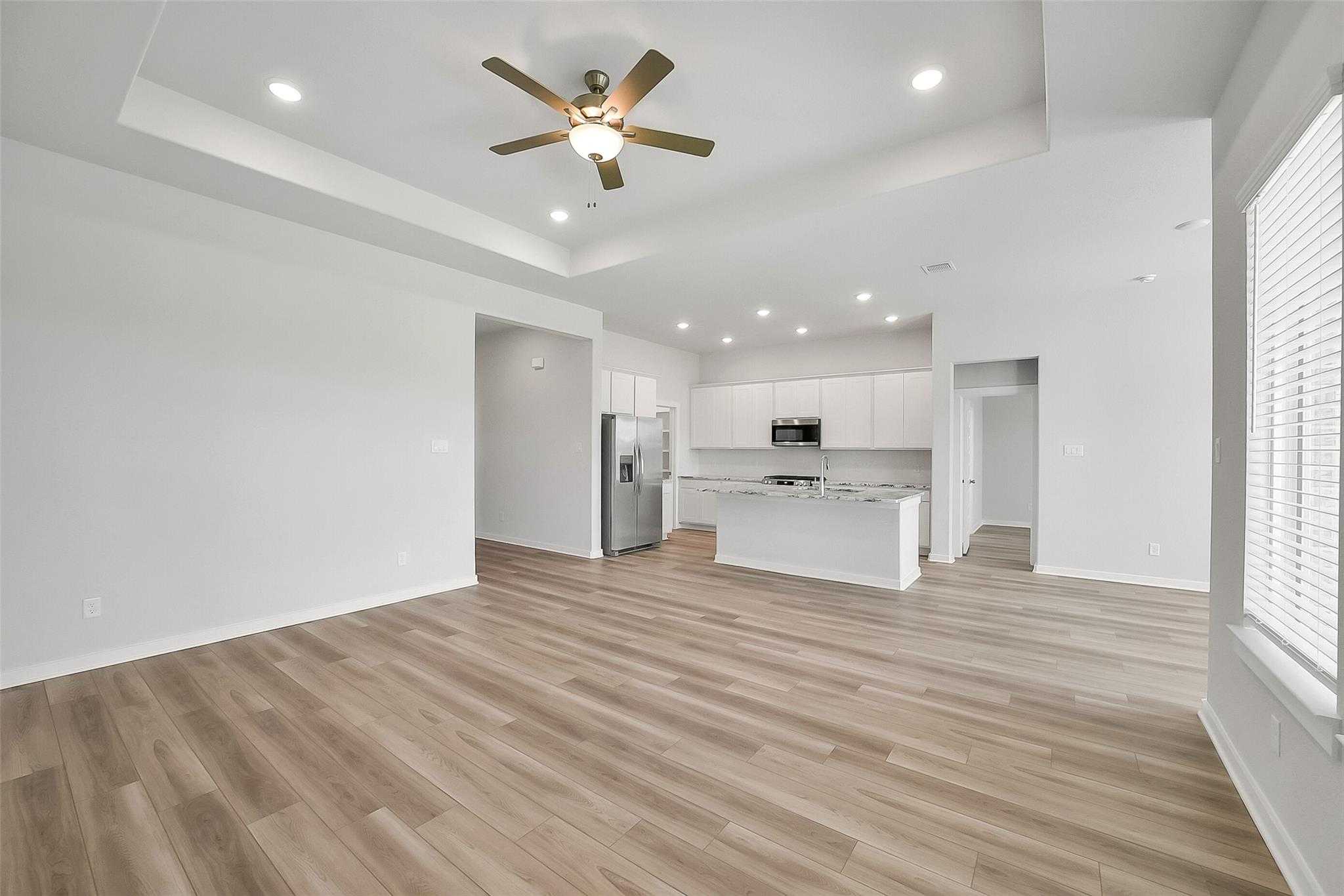 Open-concept kitchen and living room with white cabinets, stainless steel appliances, island, wood flooring, and ceiling fan in Davidson Homes Acadia A, Katy Texas