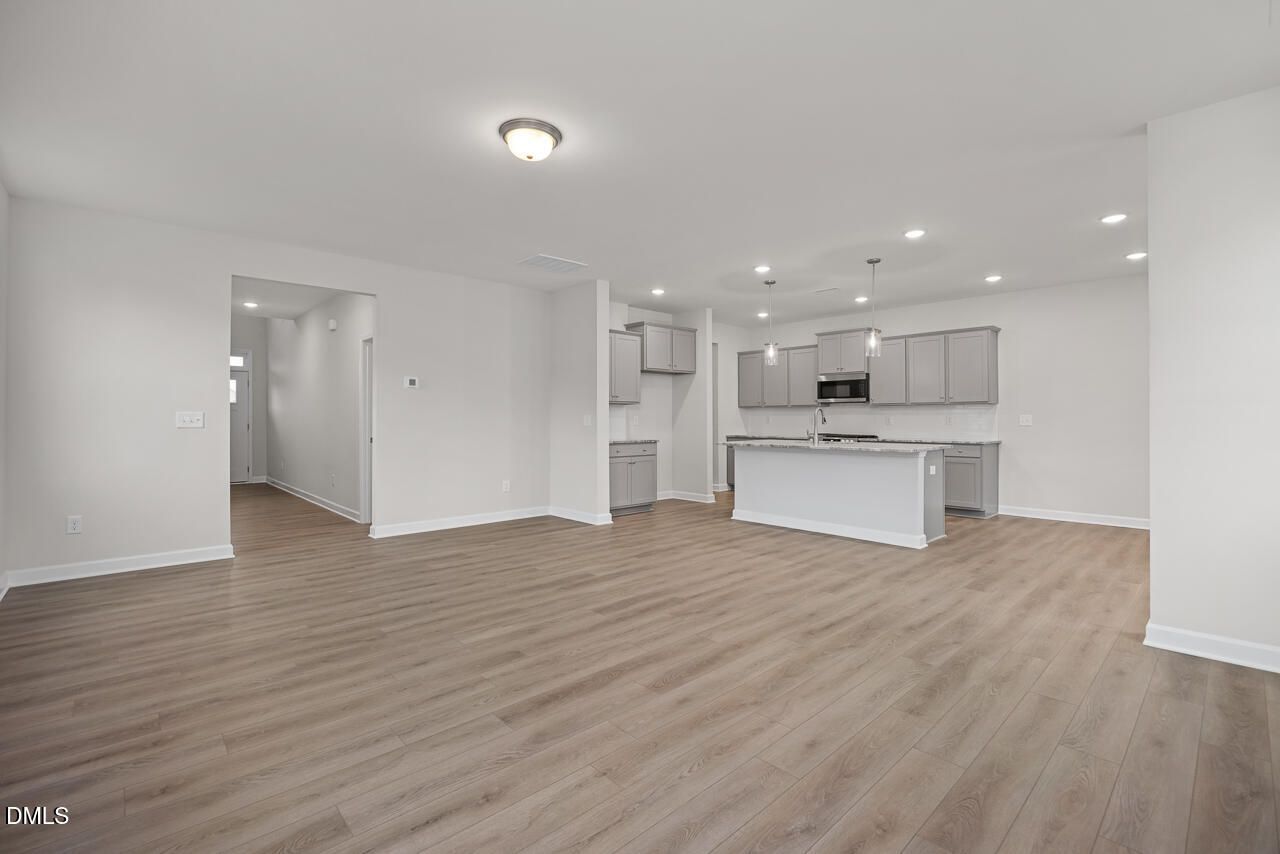 Open-concept kitchen with white shaker cabinets, quartz island, and hardwood floors in The Gavin B home, Lillington, NC