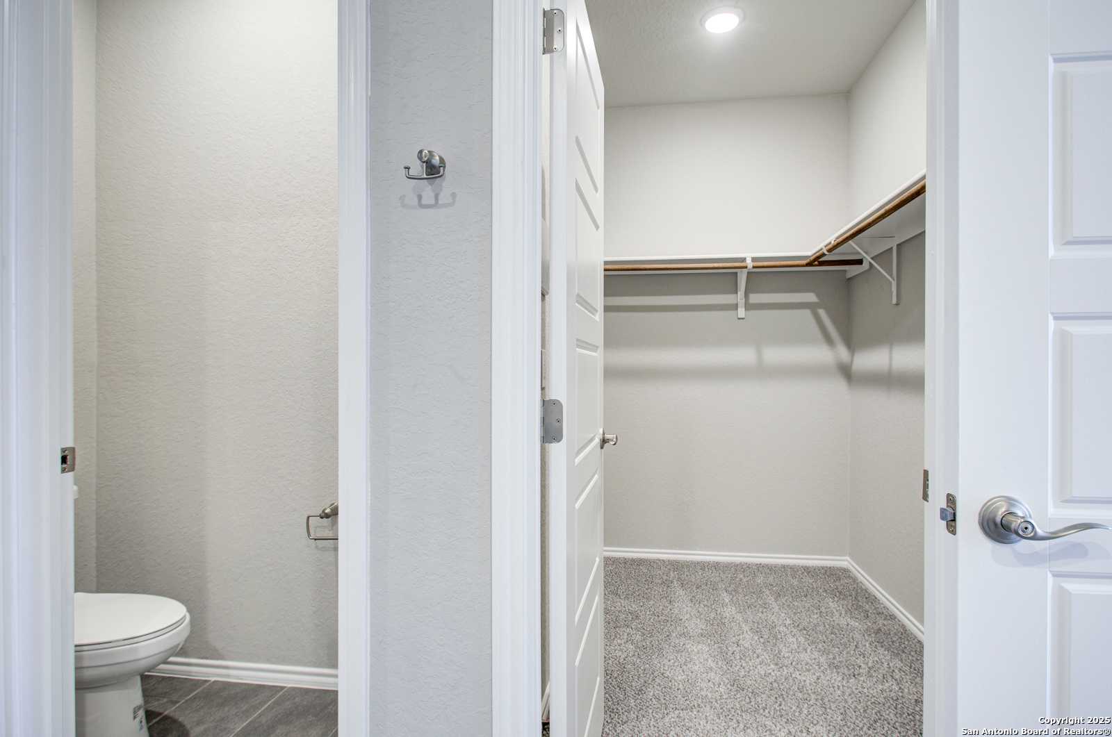 Master bathroom with white toilet and adjacent walk-in closet with shelves in Davidson Homes The Douglas G, San Antonio, Texas