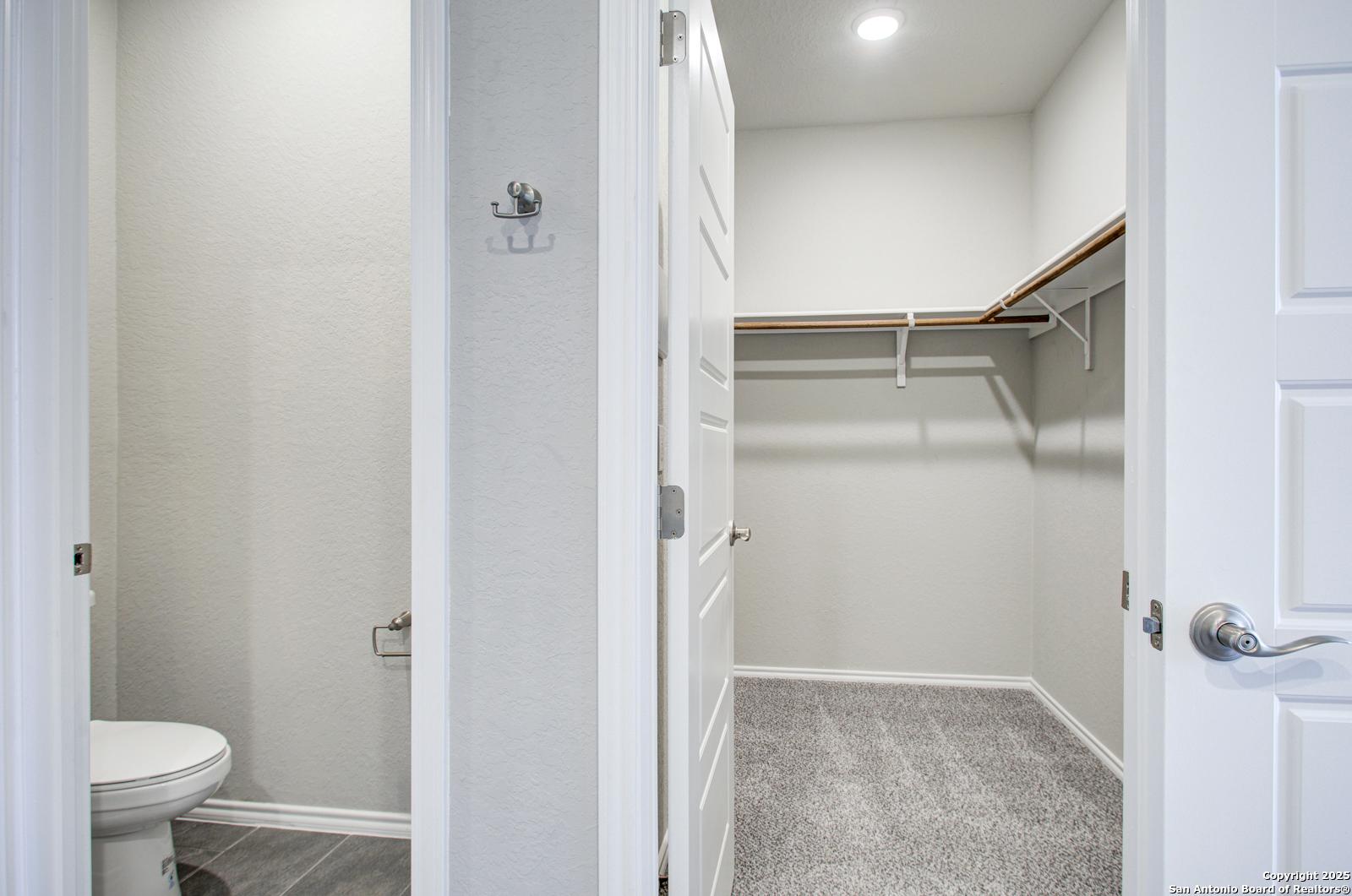 Master bathroom with white toilet and adjacent walk-in closet with shelves in Davidson Homes The Douglas G, San Antonio, Texas