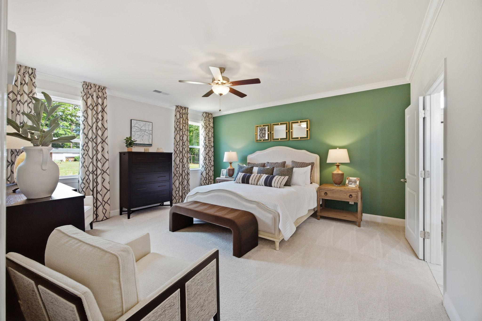 Spacious primary bedroom at Enclave at Belmont in Belmont NC with king bed, green accent wall, ceiling fan, and window views