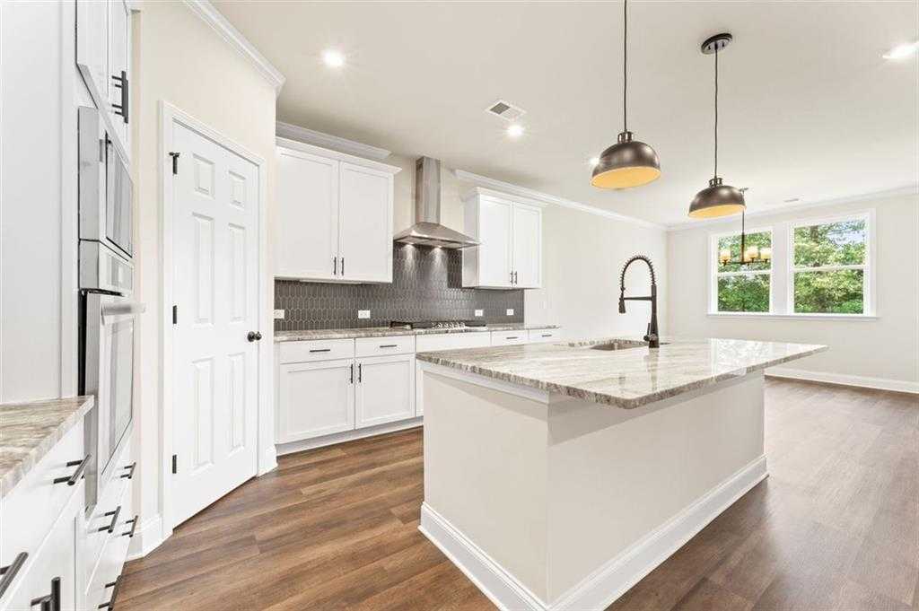 Open-concept kitchen with white shaker cabinets, granite island, stainless appliances, and pendant lights in Davidson Homes The Harrison G, Hoschton, GA