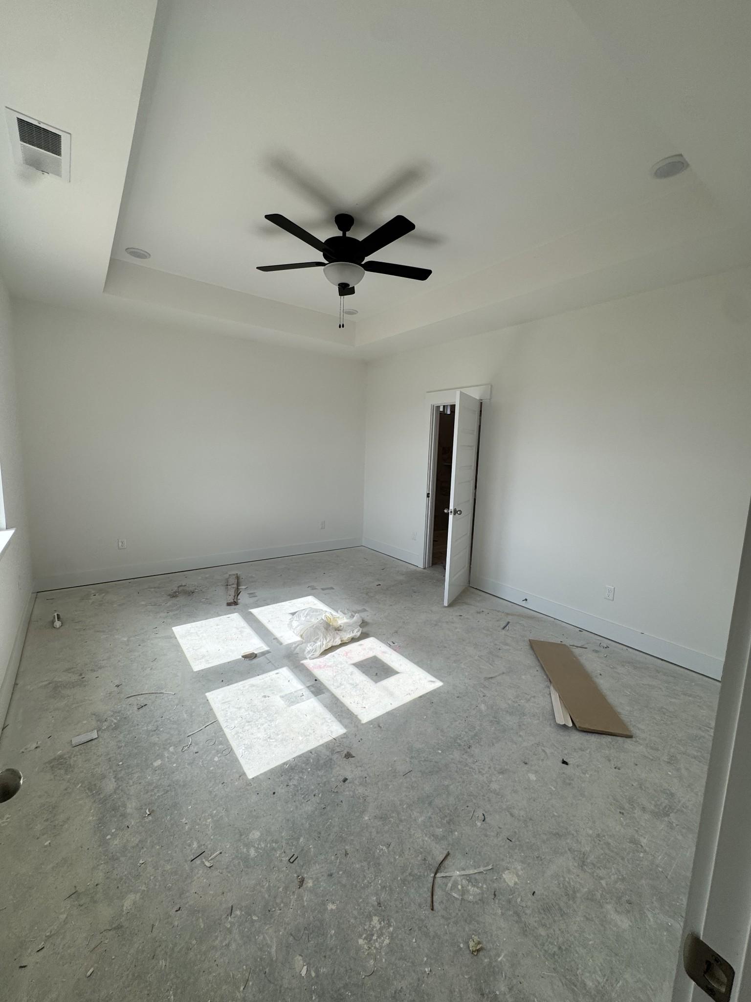 Unfinished bedroom with white walls, ceiling fan, open door, and sunlight through windows in Davidson Homes Prairie C, Gallatin, TN
