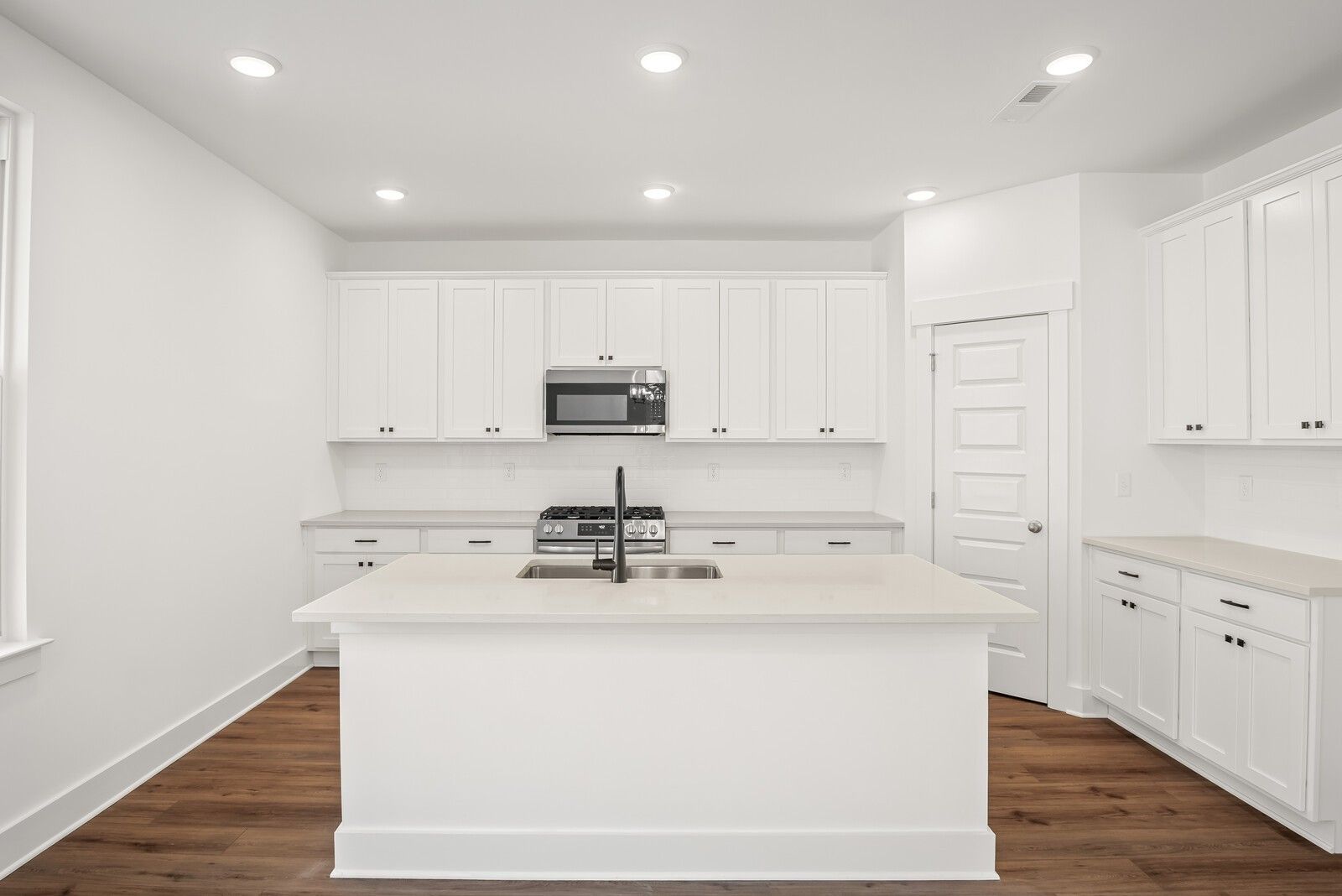 Modern white kitchen with large island sink, gas stove, microwave, and hardwood floors in The Logan C by Davidson Homes, Gallatin, TN