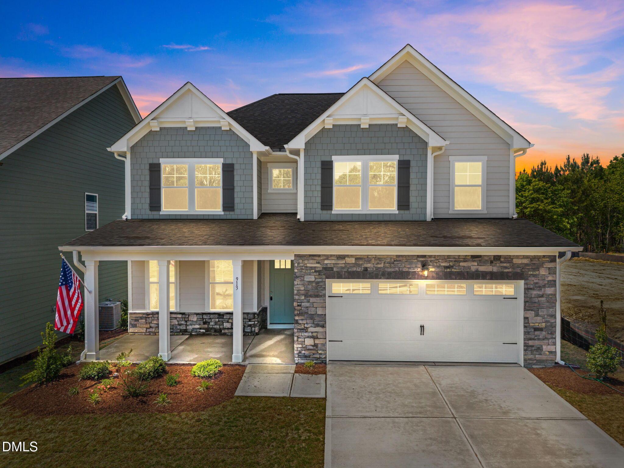 Two-story Willow D home by Davidson Homes in Wendell Ridge, gray siding, stone accents, covered porch, two-car garage at dusk, Wendell, NC