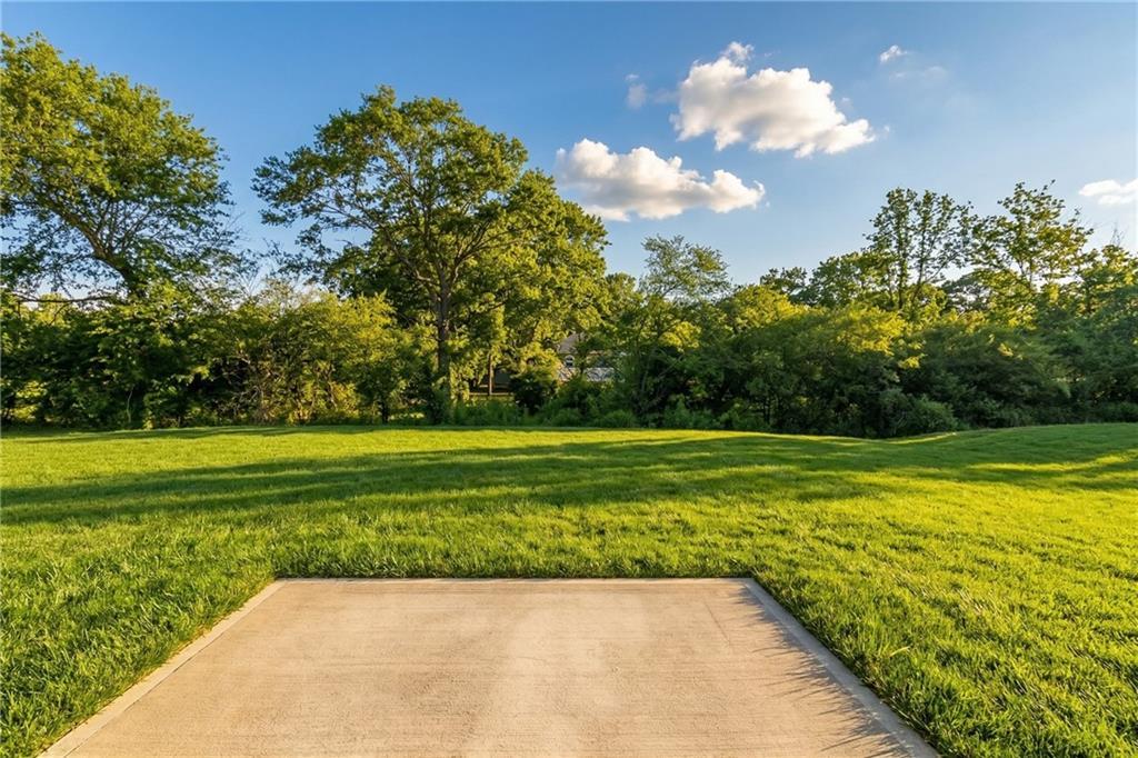 Private backyard with concrete patio slab, lush green lawn, mature trees, and blue skies in Cedar Farms 5-bedroom home, Winder, Georgia