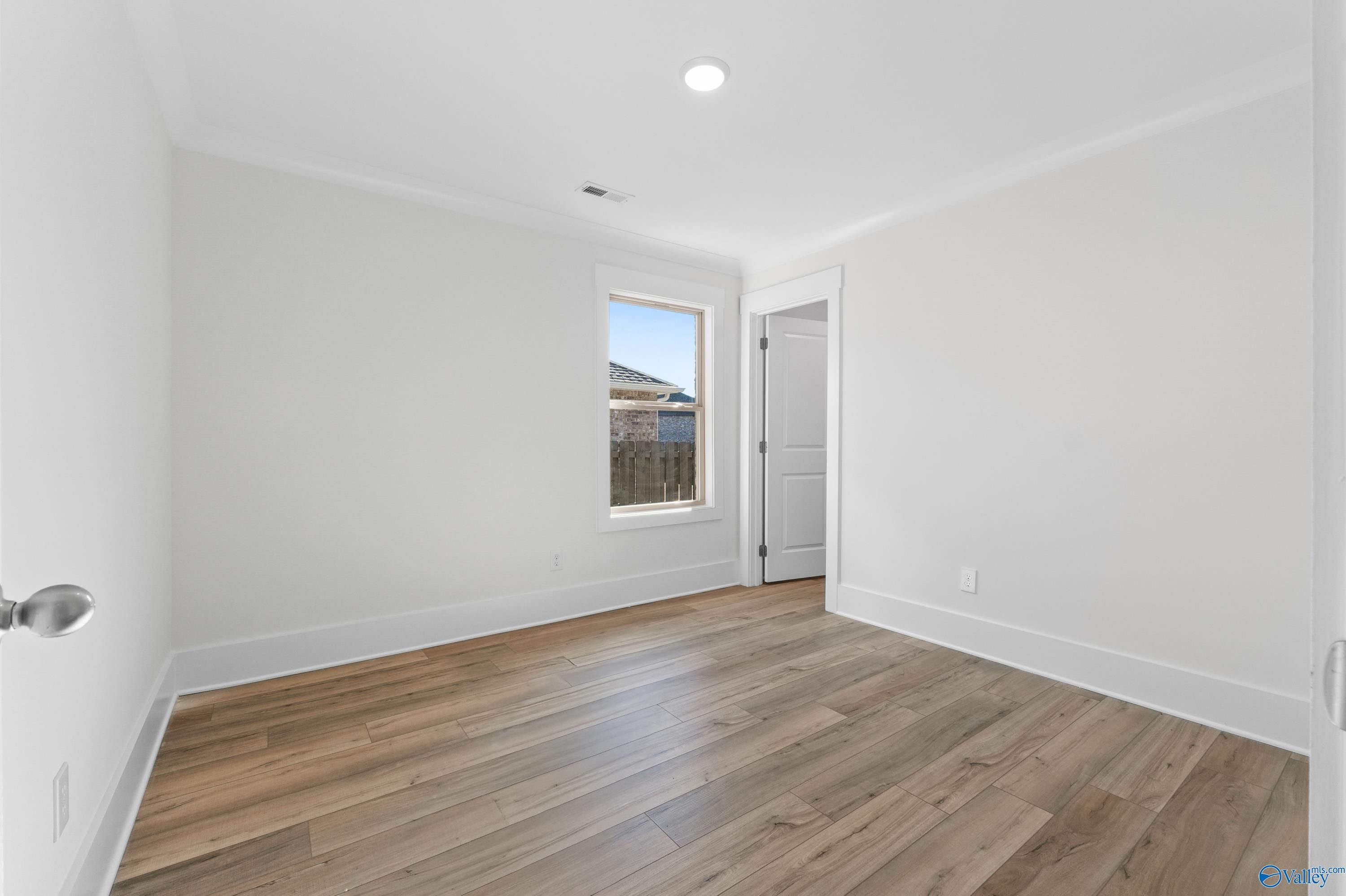 Bright empty secondary bedroom with hardwood floors, white walls, and large window in Davidson Homes The Daphne C, Arab, Alabama