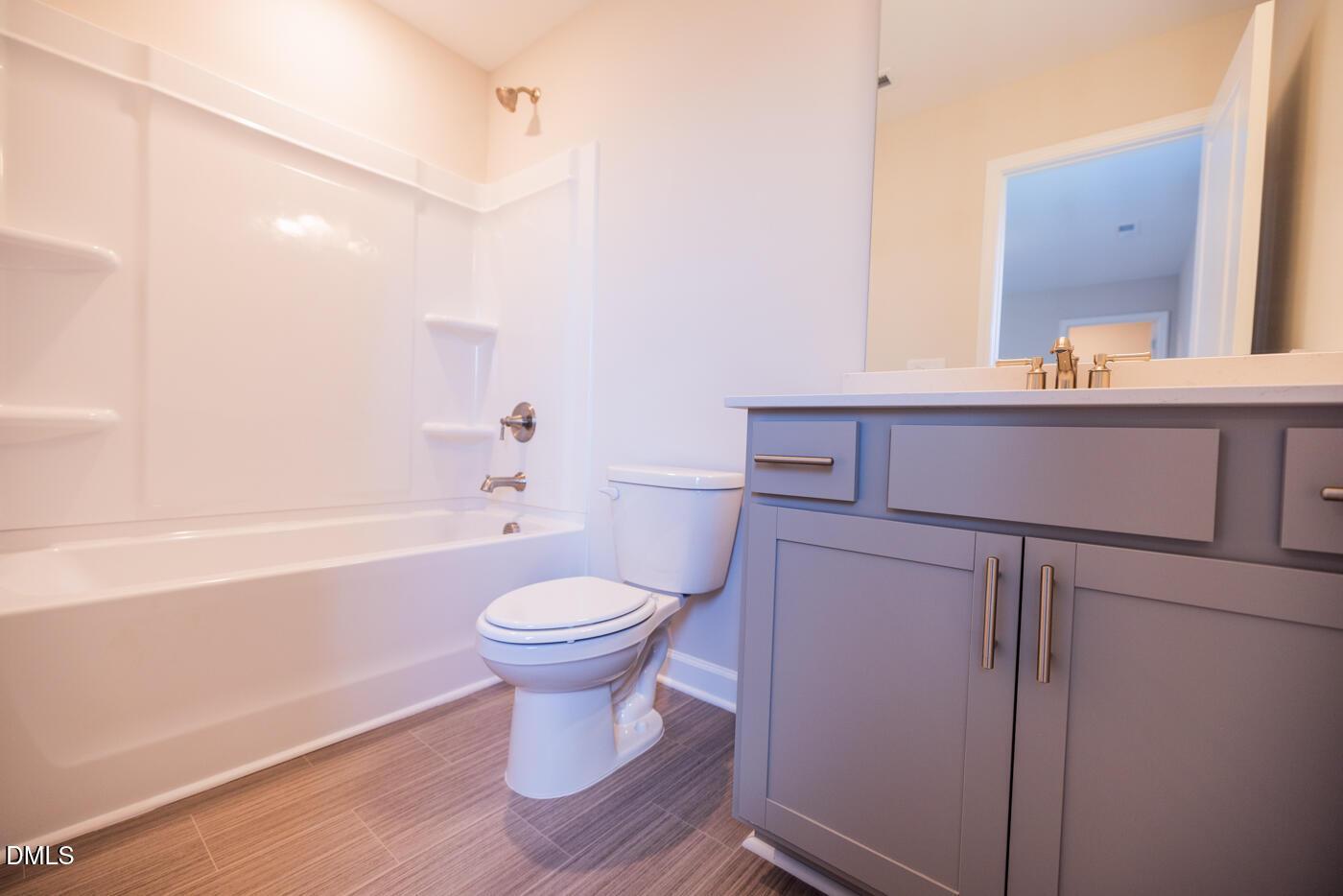 Modern bathroom with bathtub-shower combo, gray vanity, and toilet in 4-bedroom Hickory II C home, Woodland Crossing, Zebulon, NC