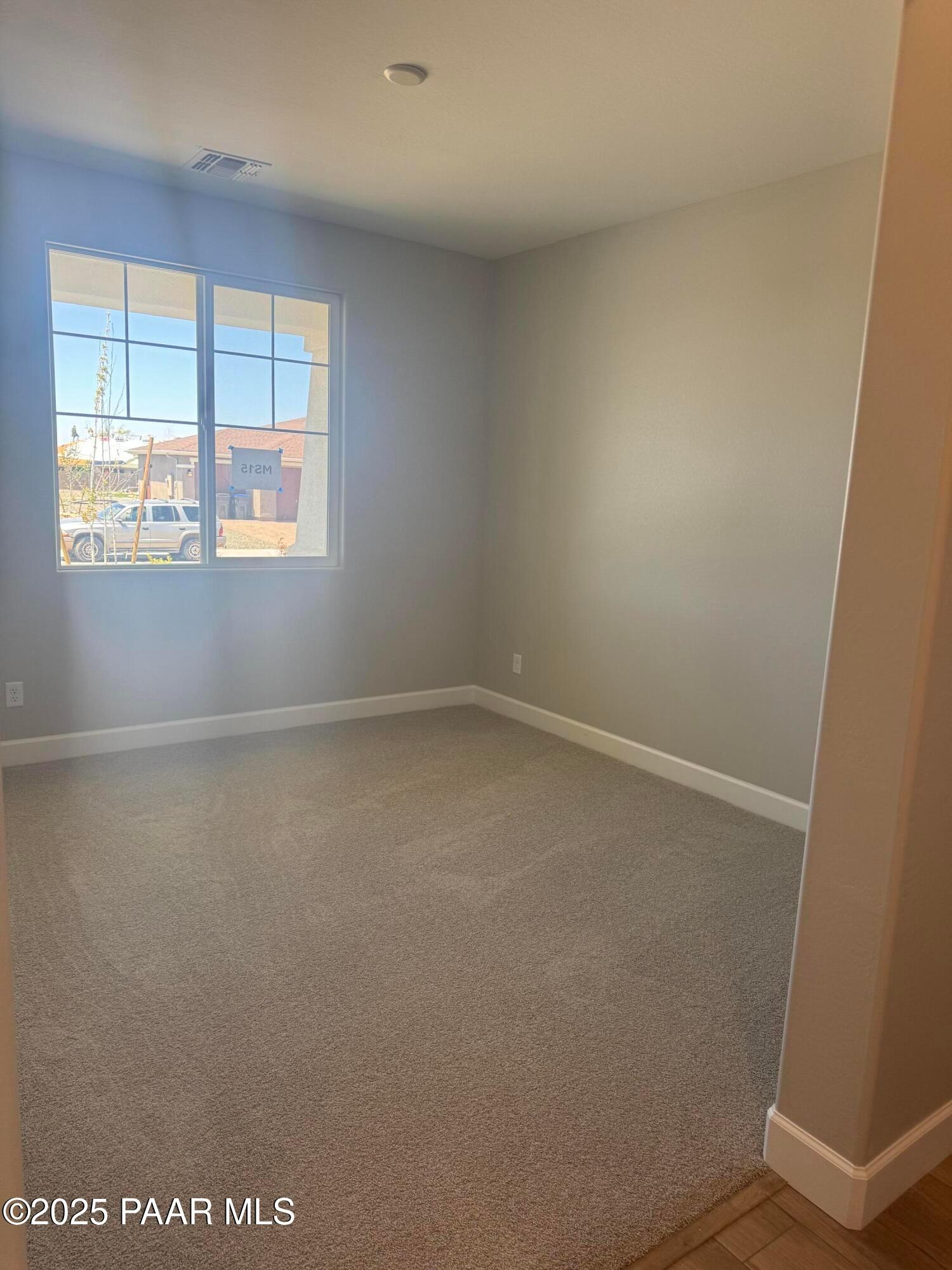 Bright empty bedroom with large sunny window, gray walls, and carpet floor in The Summit B, Evermore Homes, Prescott Valley, AZ