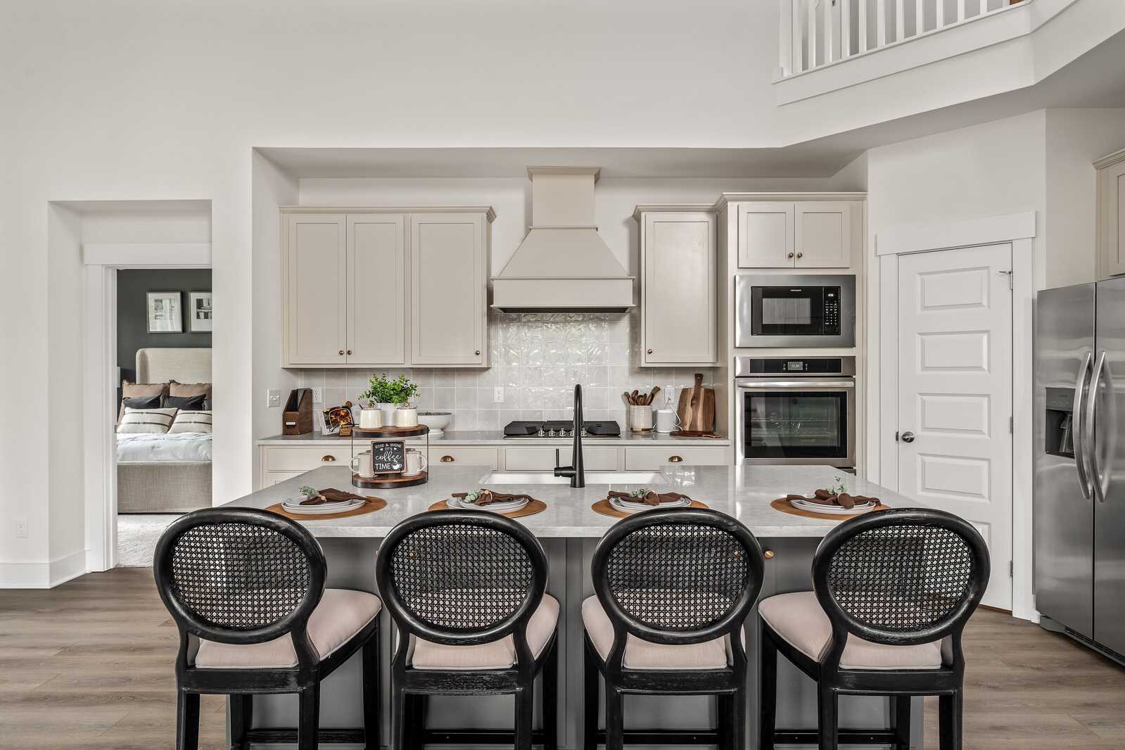 Modern white kitchen with shaker cabinets, large island, black rattan stools, stainless appliances at Woods Crossing in Gallatin TN