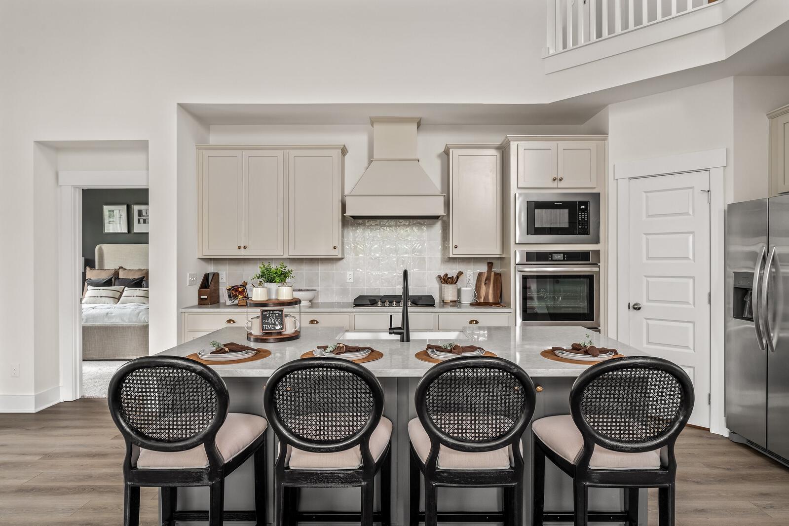 Modern white kitchen with shaker cabinets, large island, black rattan stools, stainless appliances at Woods Crossing in Gallatin TN