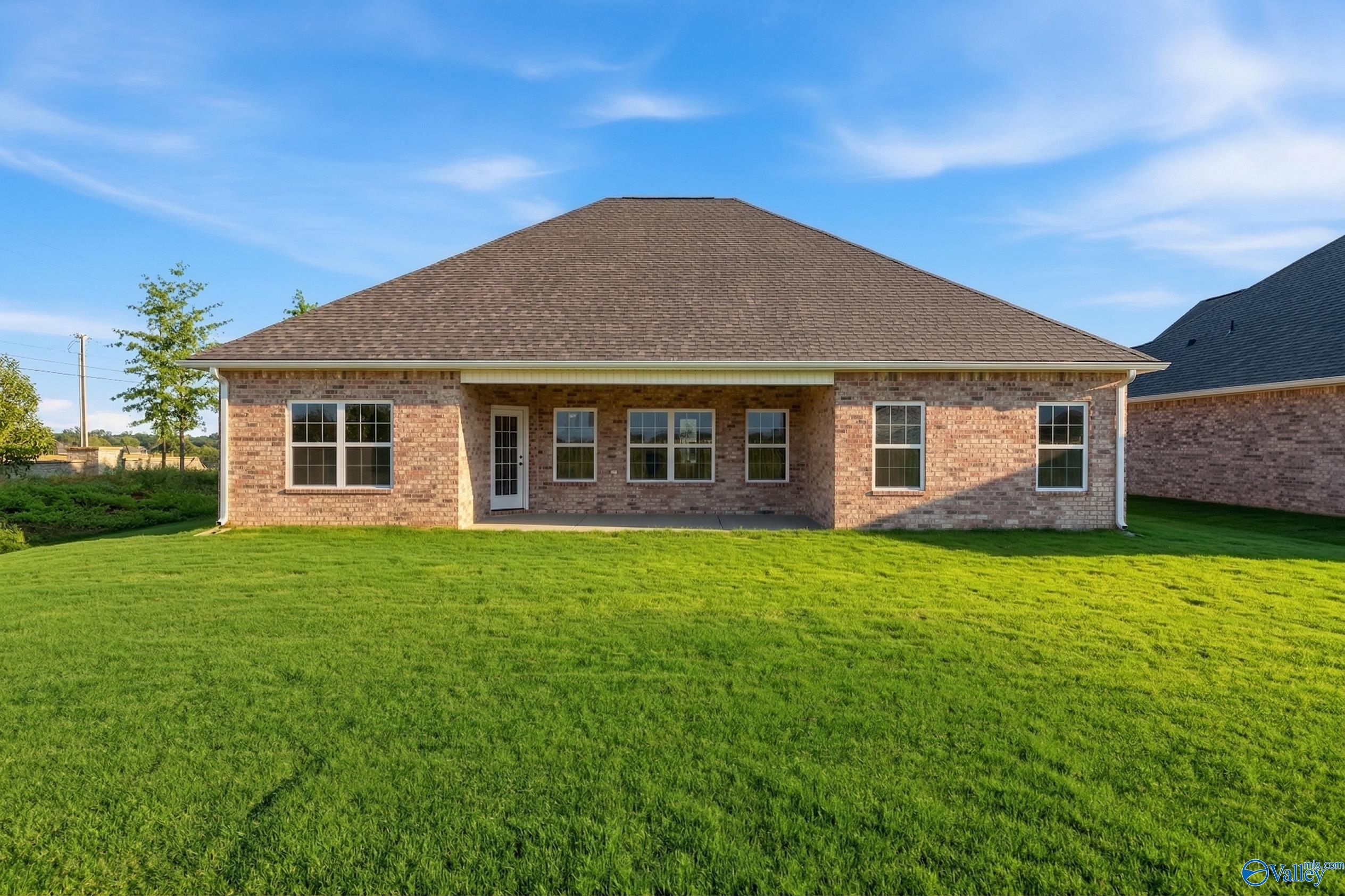 Rear brick exterior of The Rockford 3-bedroom home with covered patio, large windows, and lush green backyard in Creekside, Harvest, Alabama