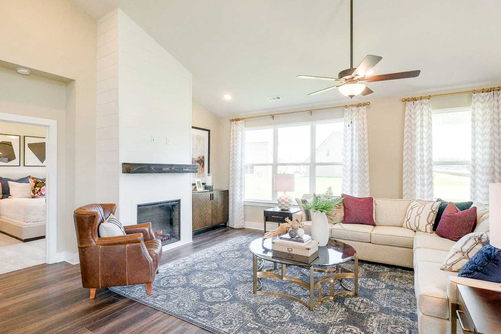 Cozy open-concept living room at The Meadows in Smyrna TN with beige sofa, leather armchair, gas fireplace, and large windows