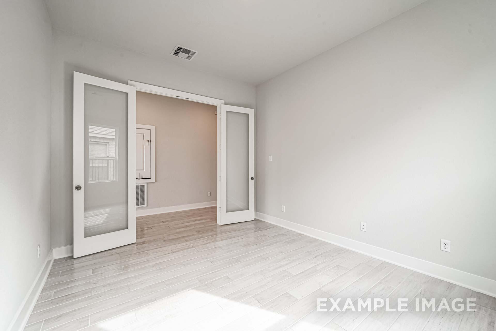 Spacious entryway in The George A home design with open French doors, light gray walls, and hardwood-look flooring