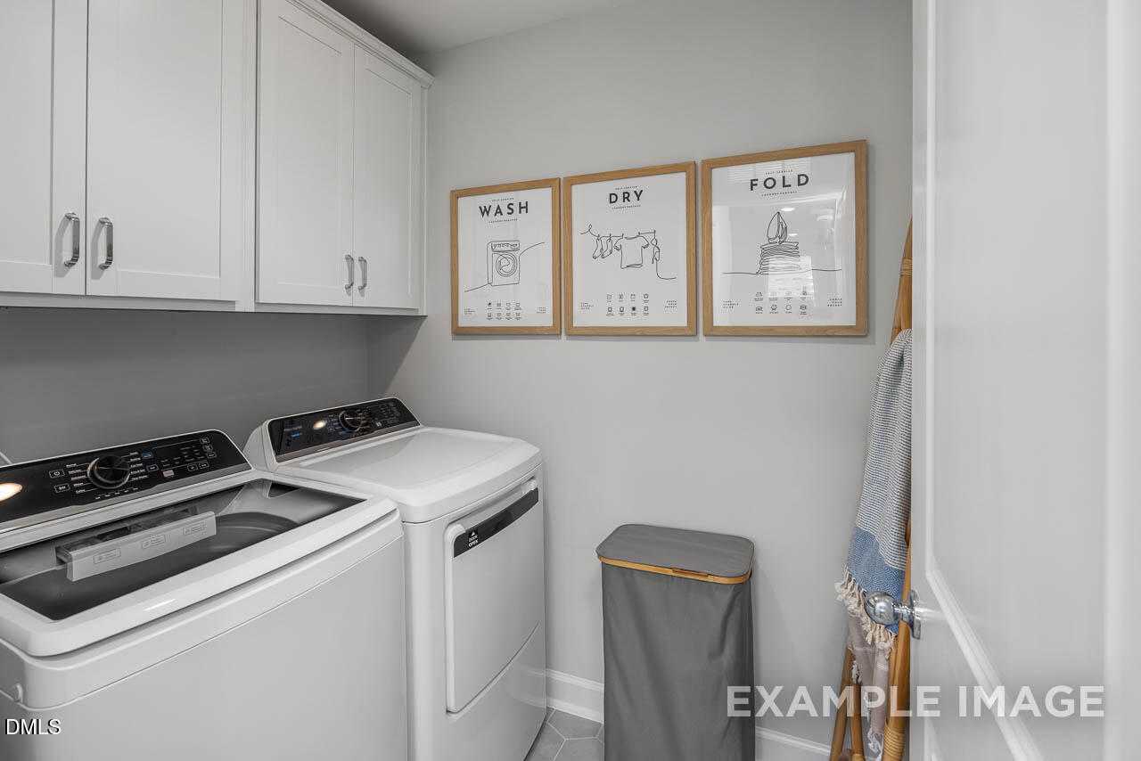 Modern laundry room with white washer, dryer, cabinets, and wash-dry-fold wall art in Davidson Homes The Graham, Fuquay-Varina, NC