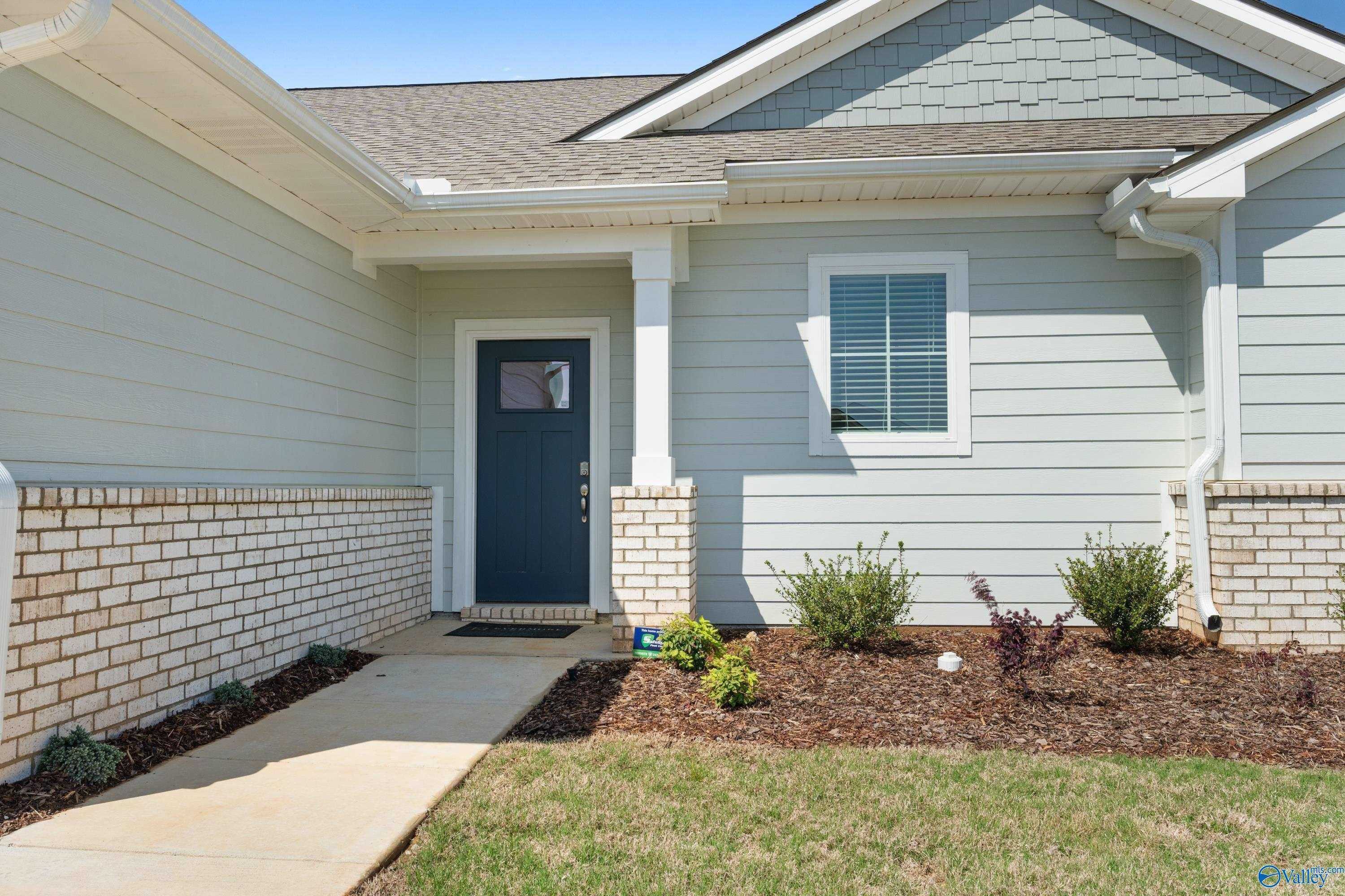 Light blue sided one-story home with brick accents, dark blue door, and landscaped front yard in Evergreen Mill, Madison, Alabama