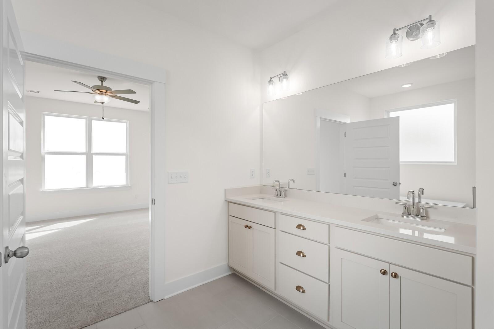 Elegant master bathroom featuring double white vanity, large mirror, sconce lights, and ceiling fan in Davidson Homes The Ridgeport, Gallatin, TN