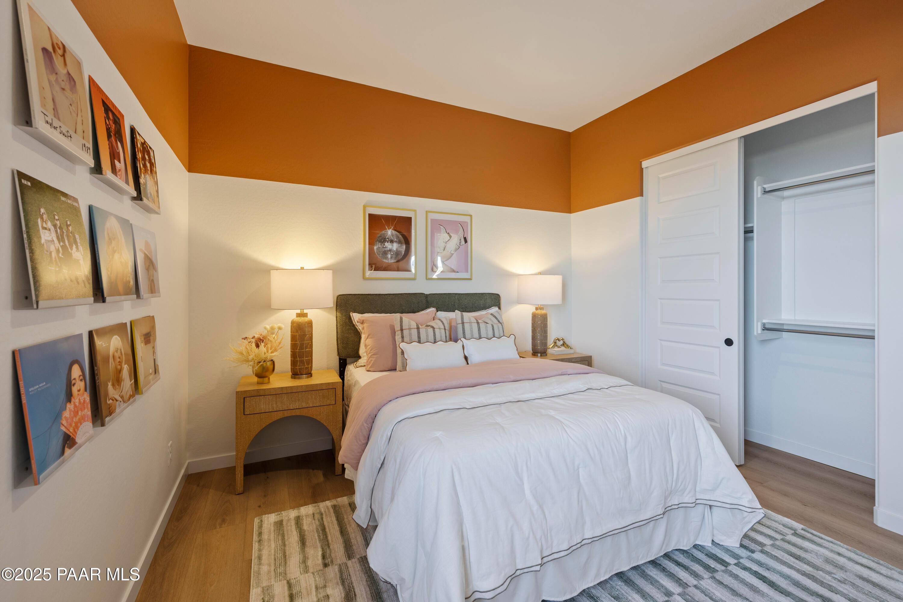 Cozy bedroom with orange accent walls, white bedding, framed art, and walk-in closet in Davidson Homes The Blaze D, Prescott, Arizona