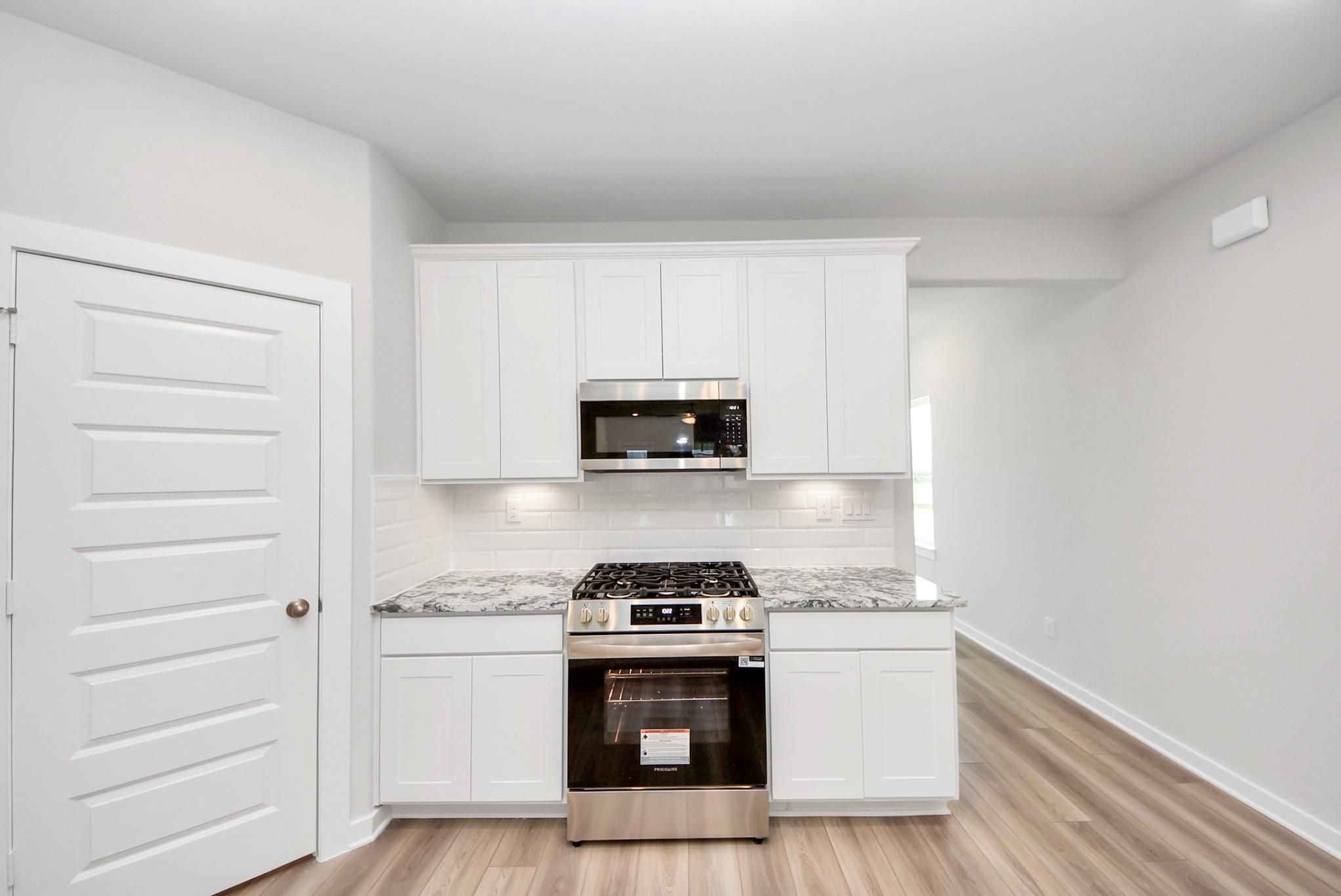 Modern kitchen with white cabinets, granite countertops, and stainless steel appliances in Sabine E home, Magnolia, Texas.