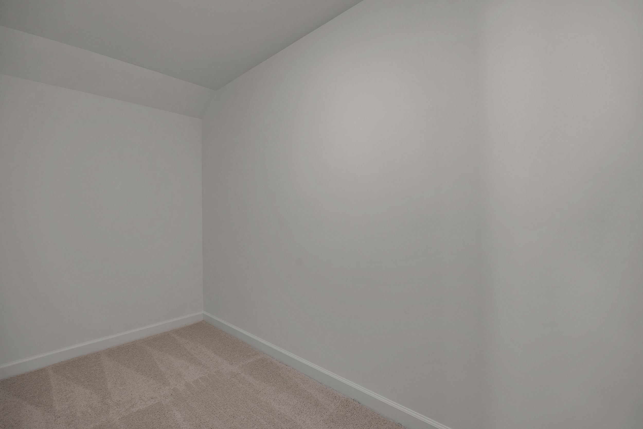Spacious empty bedroom featuring white walls and neutral carpet flooring in Sage on North Main, Wake Forest NC by Davidson Homes
