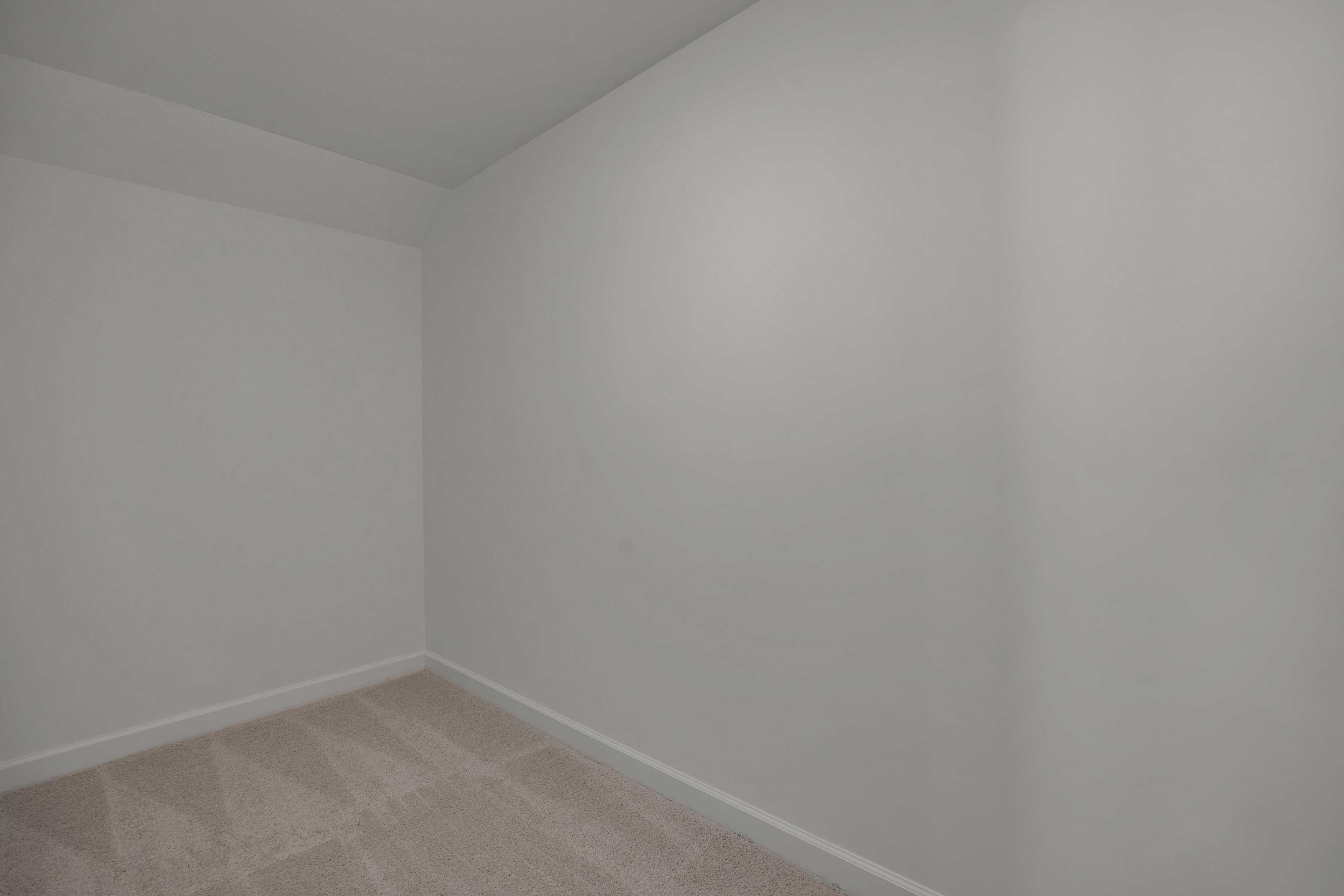 Spacious empty bedroom featuring white walls and neutral carpet flooring in Sage on North Main, Wake Forest NC by Davidson Homes