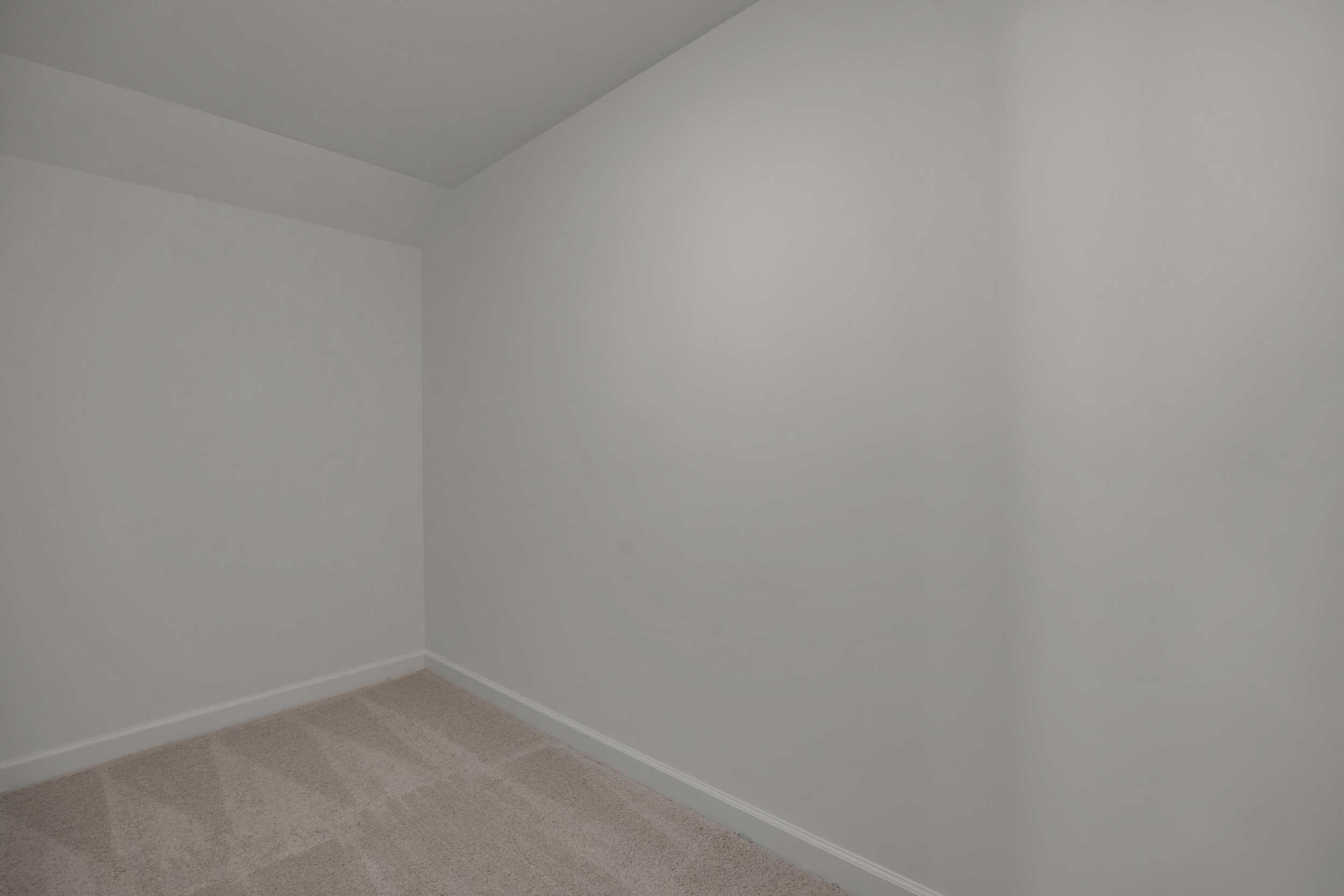 Spacious empty bedroom featuring white walls and neutral carpet flooring in Sage on North Main, Wake Forest NC by Davidson Homes