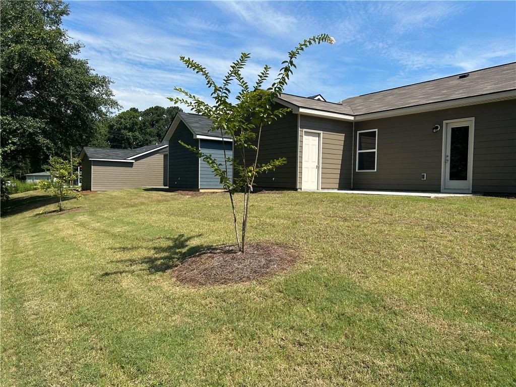 Covered back patio and lush green backyard with young tree in single-story 3-bedroom Davidson Homes The Washington, Phenix City, Alabama