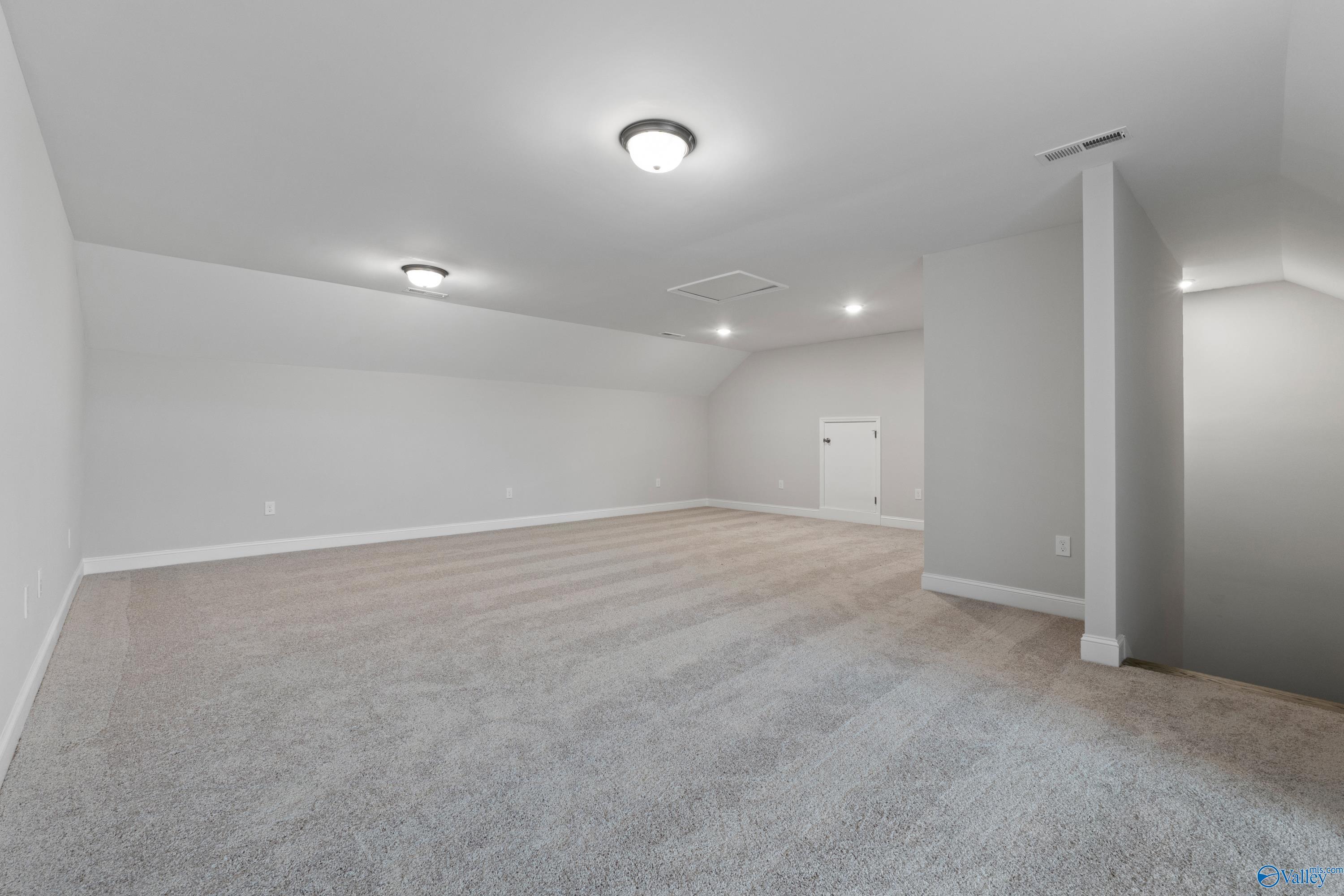Spacious bonus room with gray carpet, walls, sloped ceiling, recessed lights, stairs in Davidson Homes The Rockford B with Bonus, Toney, Alabama