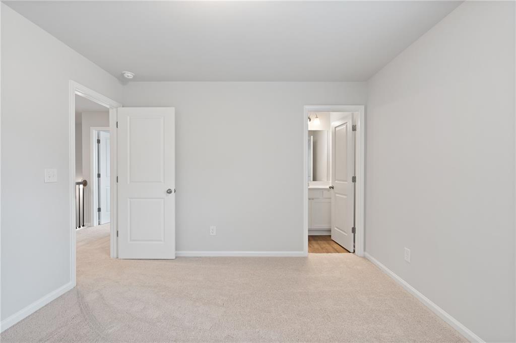 Empty bedroom with beige carpet, white walls, open bathroom door, and closet entry in 5-bedroom Davidson Homes The Hickory A, Winder, Georgia