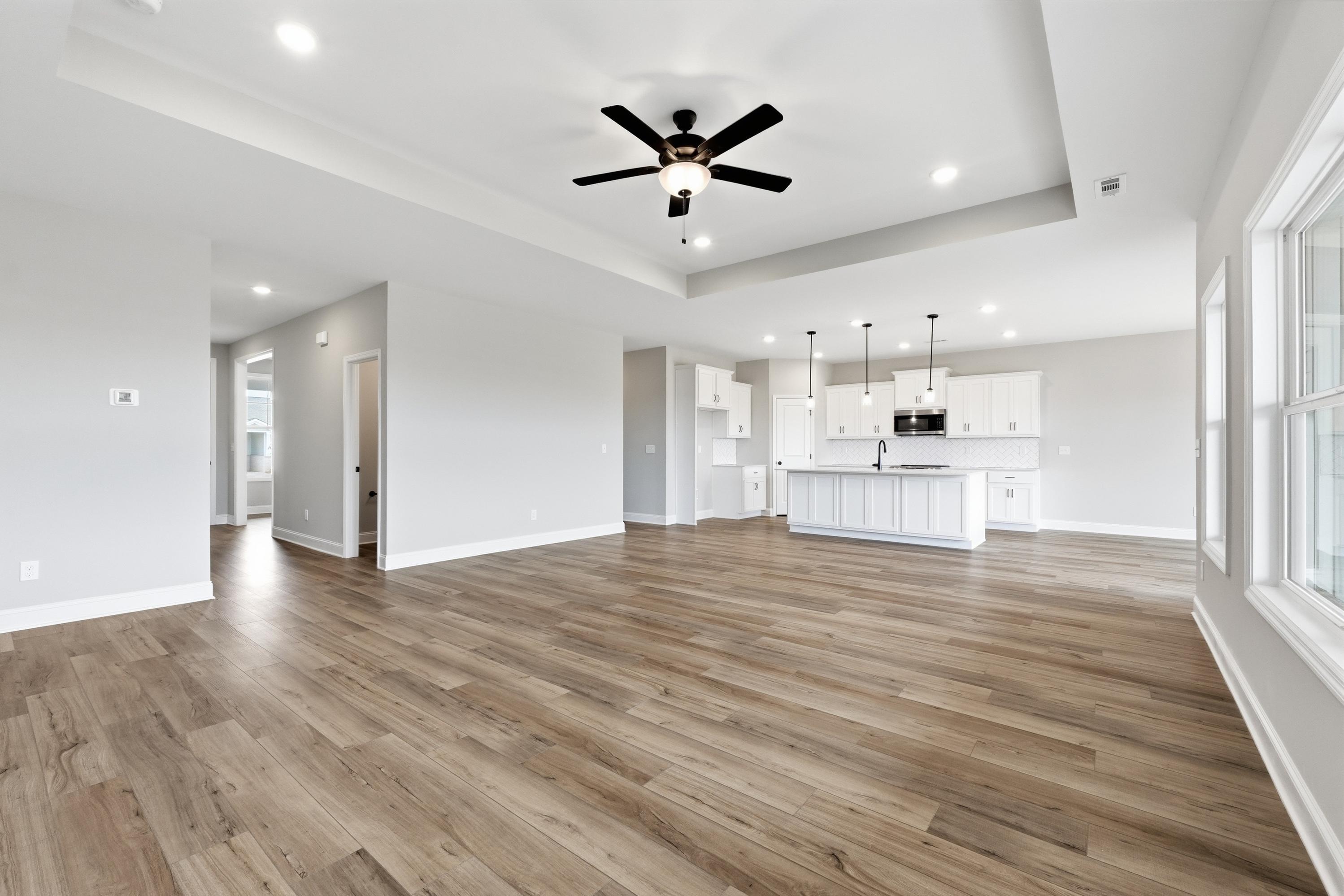 Spacious open-concept kitchen and living area in The Rockford home with hardwood floors, white island, and ceiling fan