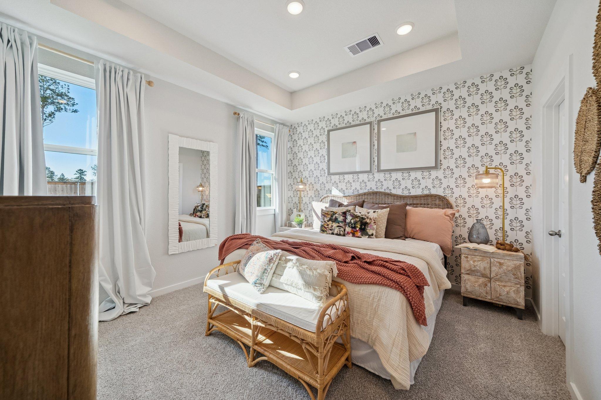 Elegant primary bedroom in Spring Branch Crossing Conroe TX with king bed, rattan bench, patterned walls and large windows