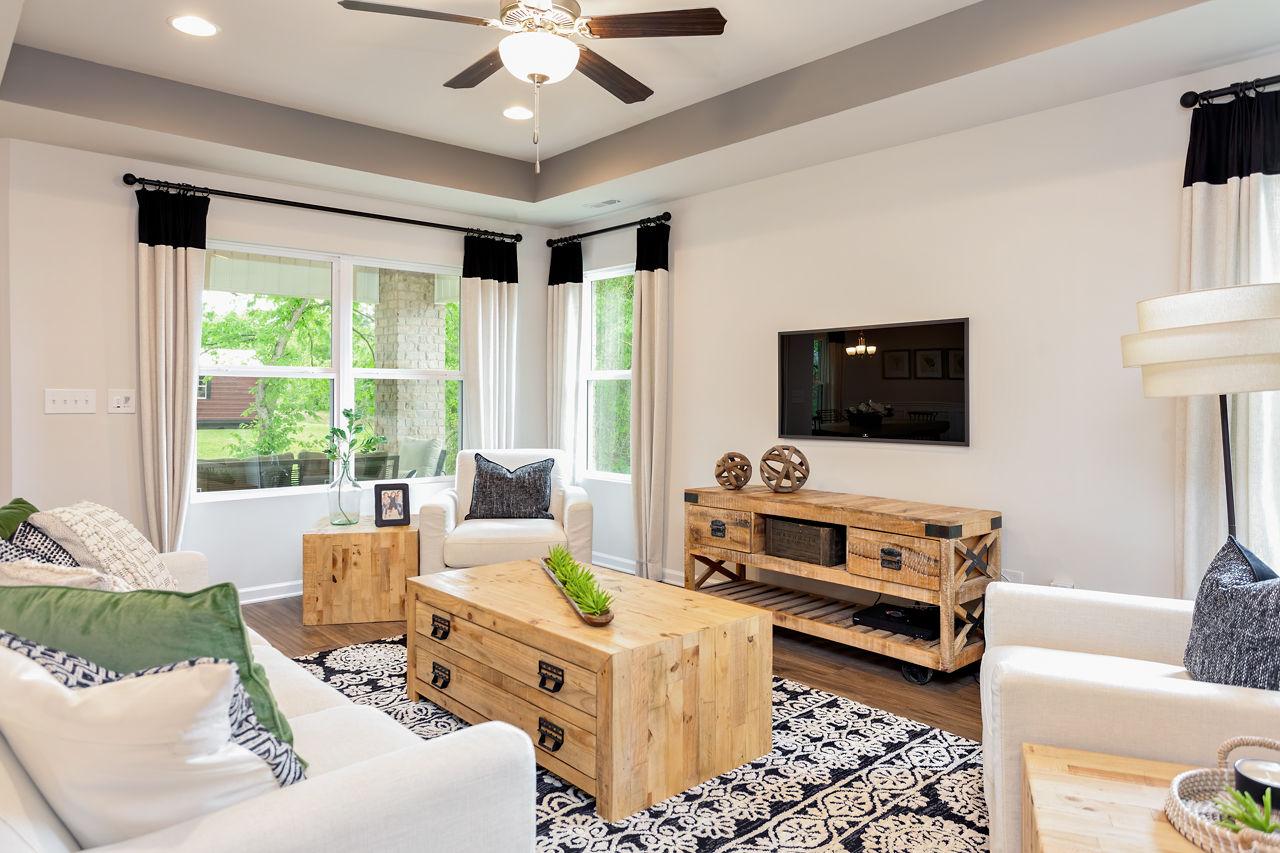Spacious living room in The Franklin C with white sofas, rustic wood coffee table, entertainment center, ceiling fan, and large windows