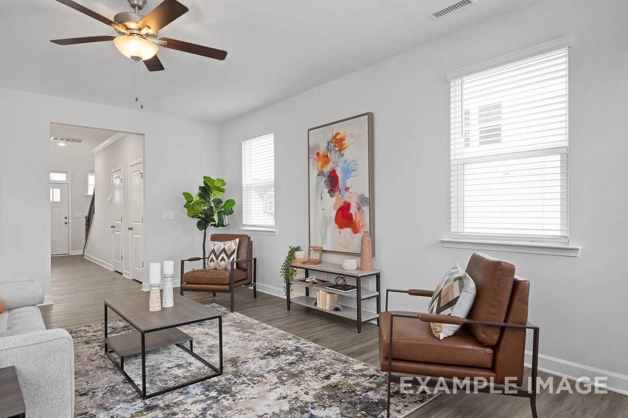 Spacious living room in The Grace A home with brown leather chairs, abstract wall art, ceiling fan, and hardwood floors