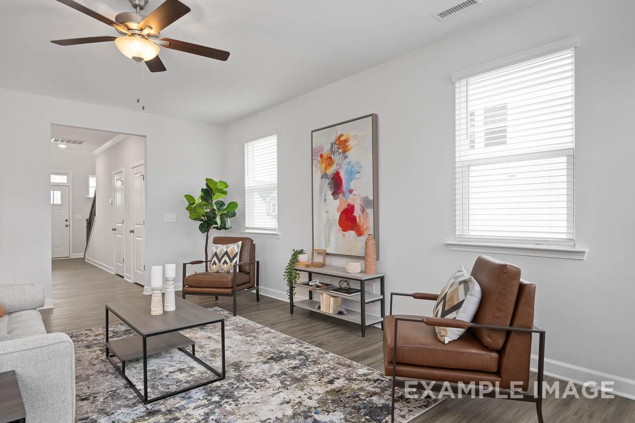 Spacious living room in The Grace A home with brown leather chairs, abstract wall art, ceiling fan, and hardwood floors
