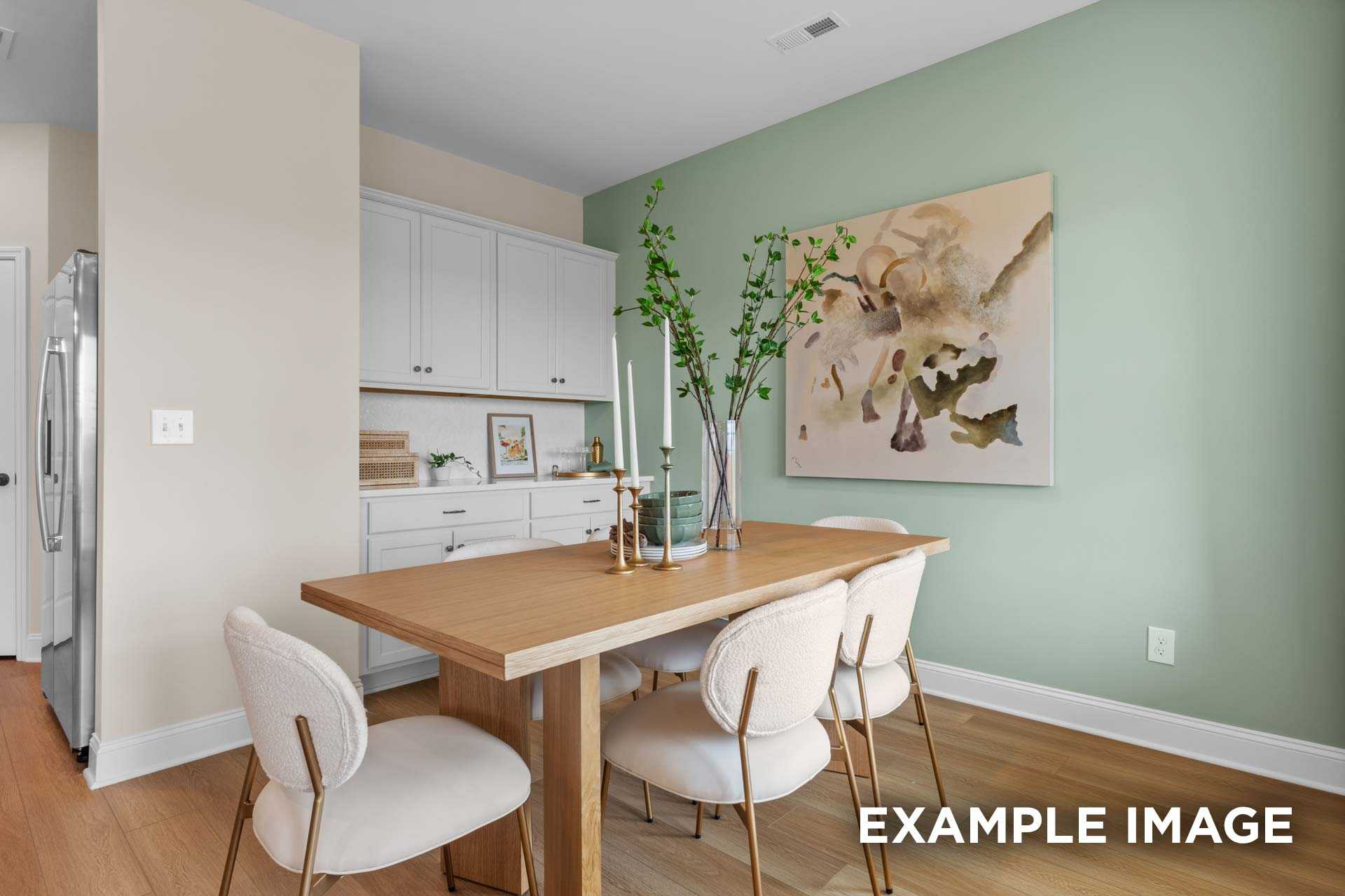 Modern dining room in The Laurel N by Davidson Homes: oak table, cream chairs, green wall, abstract art, white kitchen cabinets