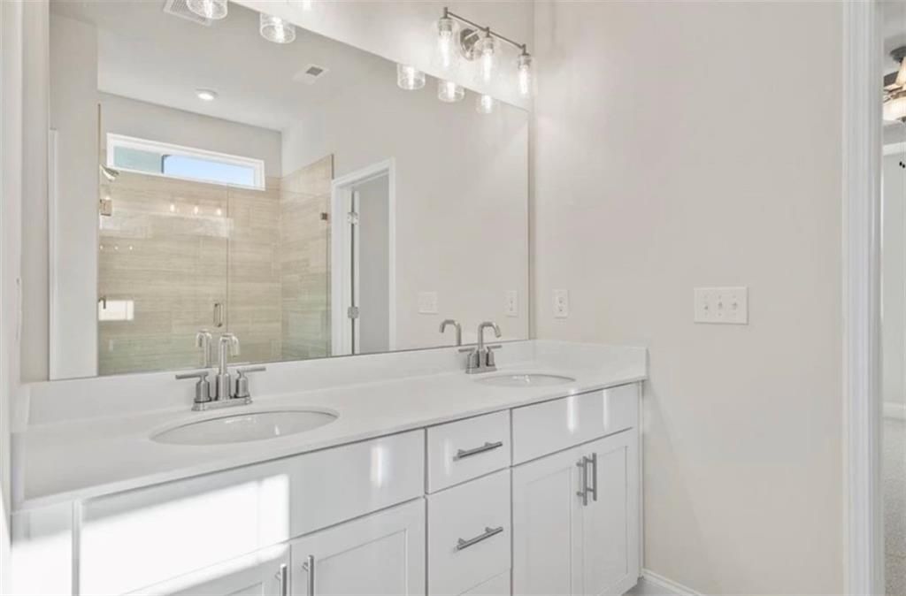 Modern double vanity with white cabinets and glass-enclosed shower in The Ash C home at Wehunt Meadows, Hoschton, Georgia.