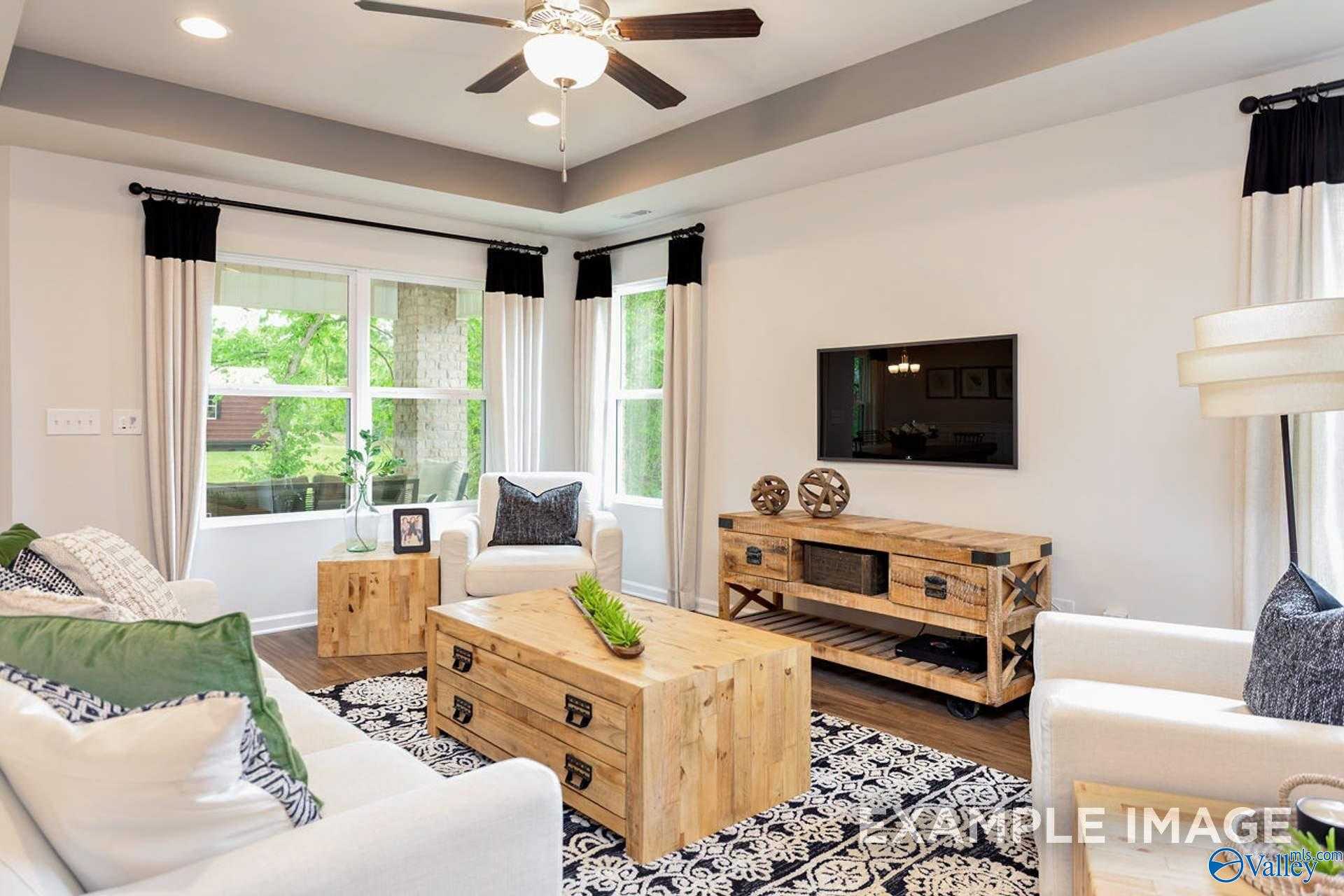 Cozy living room featuring white sectional sofa, rustic wooden tables, mounted TV, and large windows in Davidson Homes The Franklin B, Hazel Green, Alabama