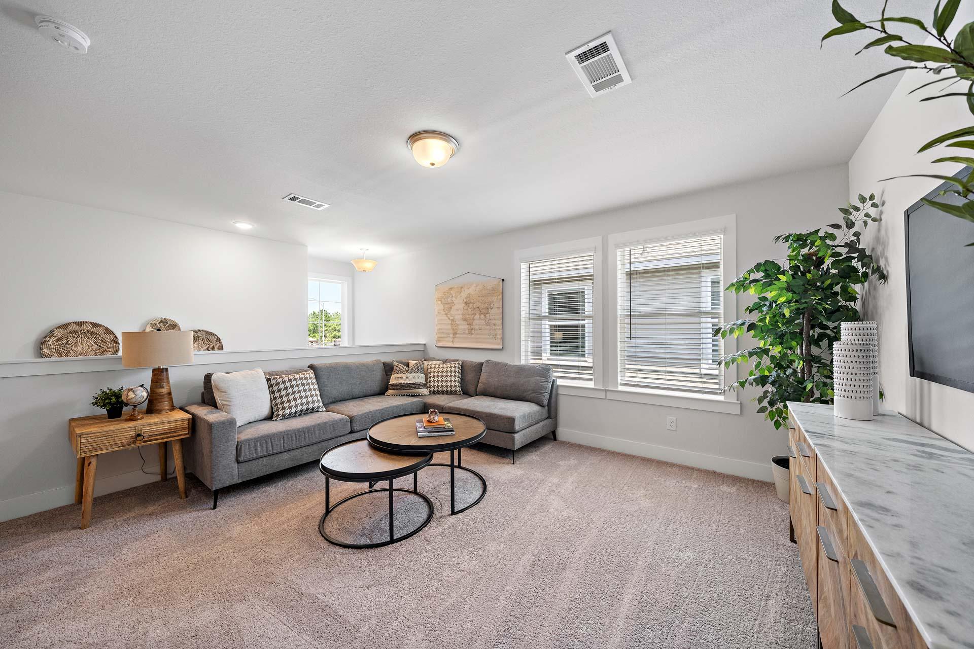 Cozy living room at Haven at Kieth Harrow in Cypress TX with gray sectional sofa, potted plants, and large windows