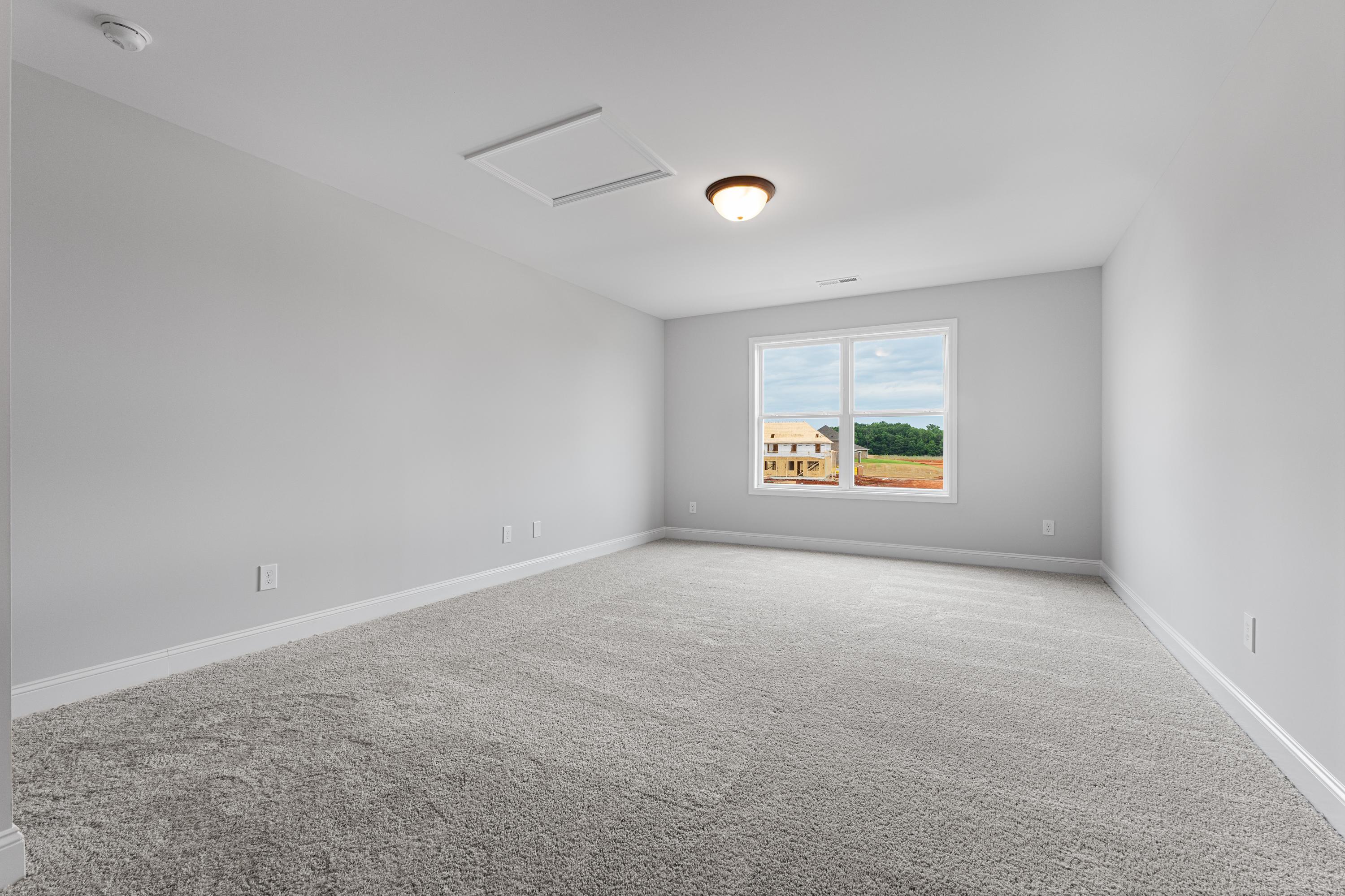 Spacious empty bedroom in The Copeland by Davidson Homes, Madison AL: gray walls, plush carpet, ceiling light, large window with neighborhood view