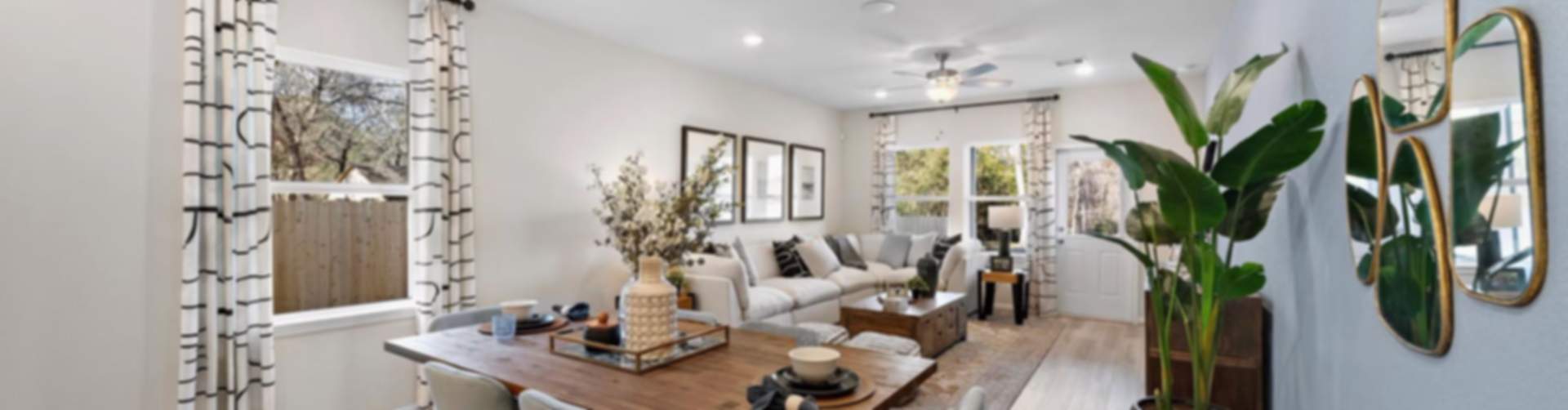 Open-concept dining and living room in modern Cibolo new home with wooden table, upholstered chairs, potted palms, mirrors, and hardwood floors