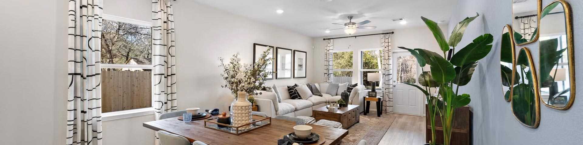 Open-concept dining and living room in modern Cibolo new home with wooden table, upholstered chairs, potted palms, mirrors, and hardwood floors