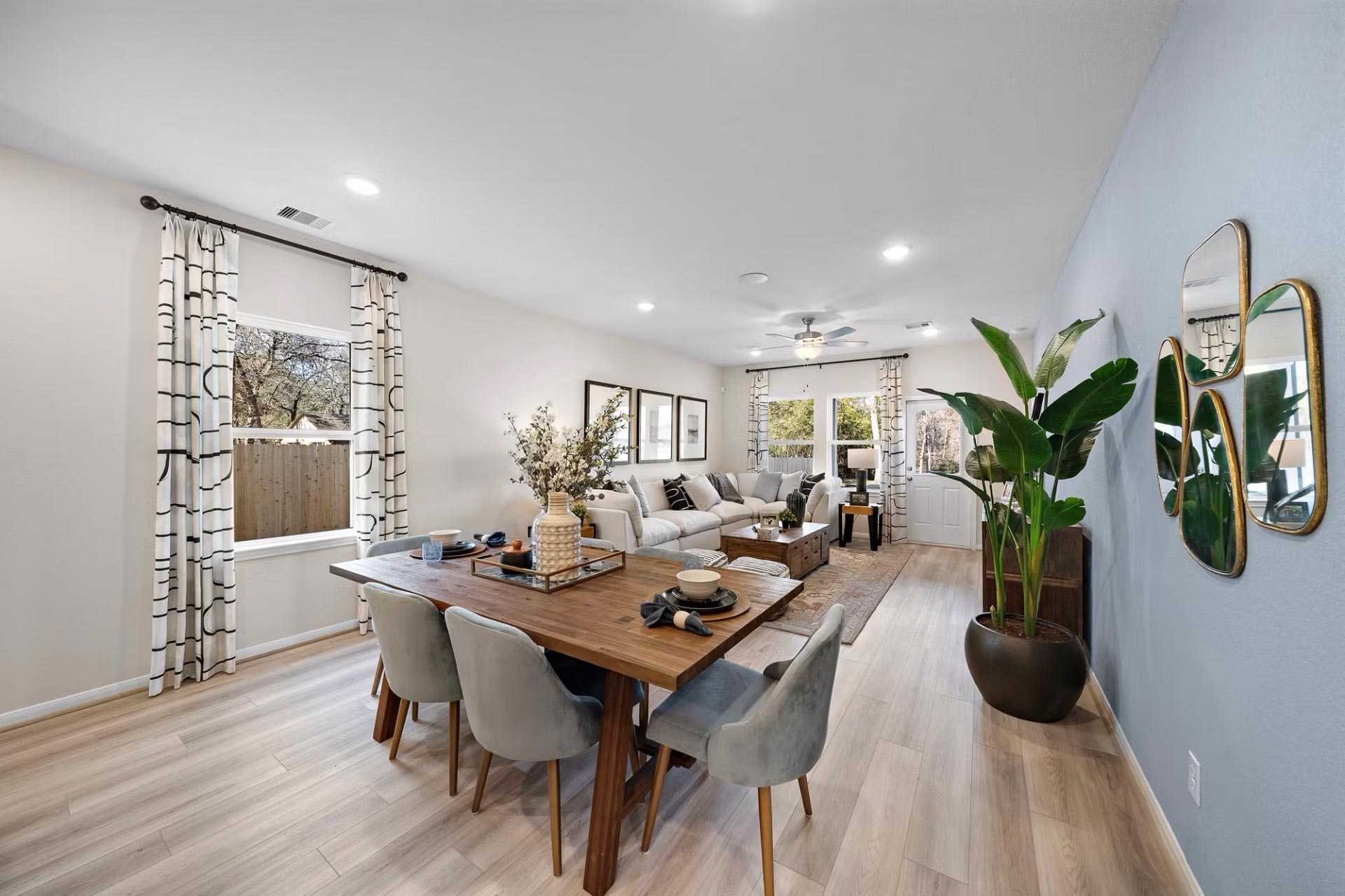 Open-concept dining and living room at Saddle Creek Ranch in Cibolo Texas with wooden table, gray sectional sofa, and potted plants