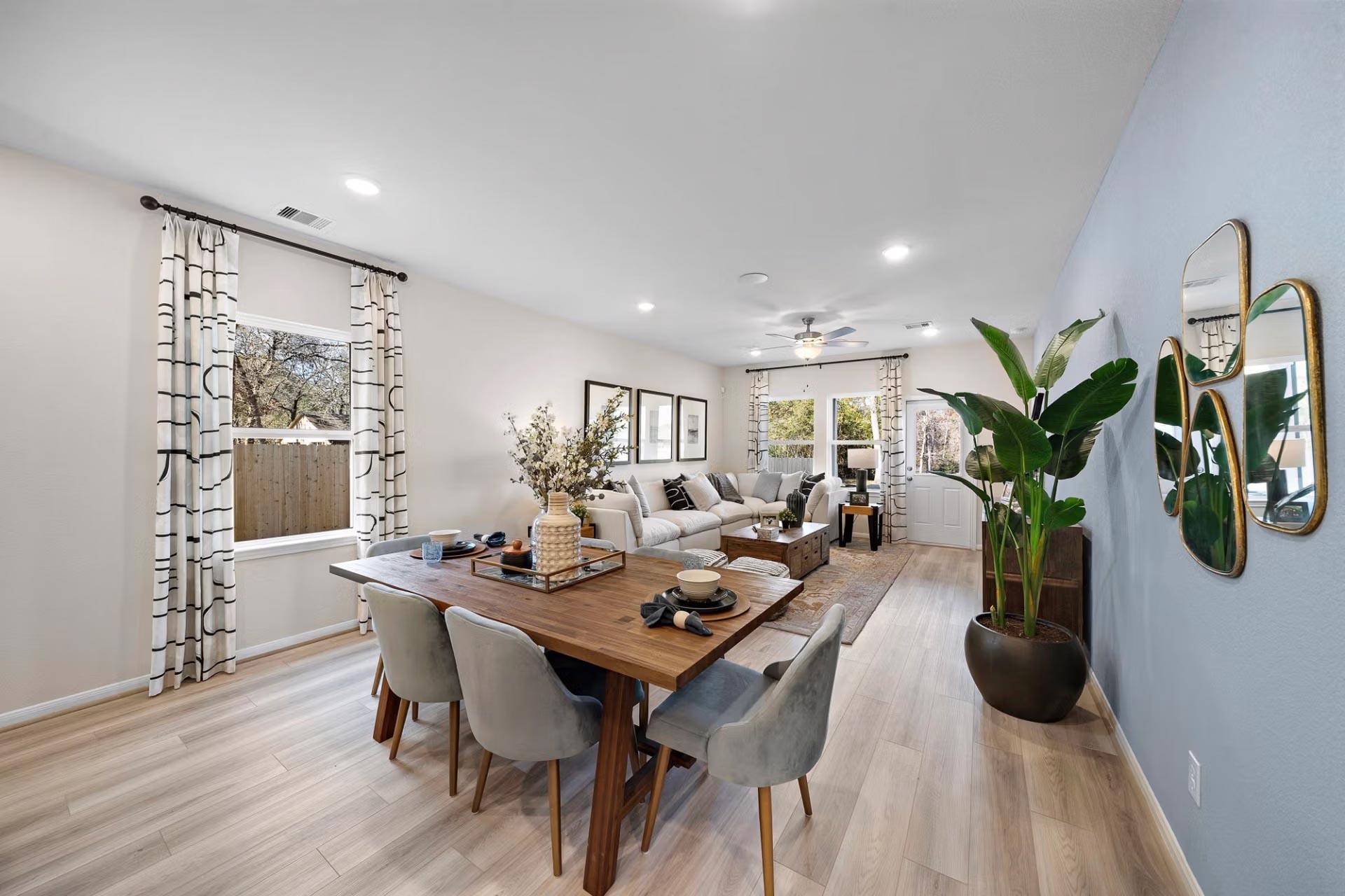 Open-concept dining and living room at Saddle Creek Ranch in Cibolo Texas with wooden table, gray sectional sofa, and potted plants