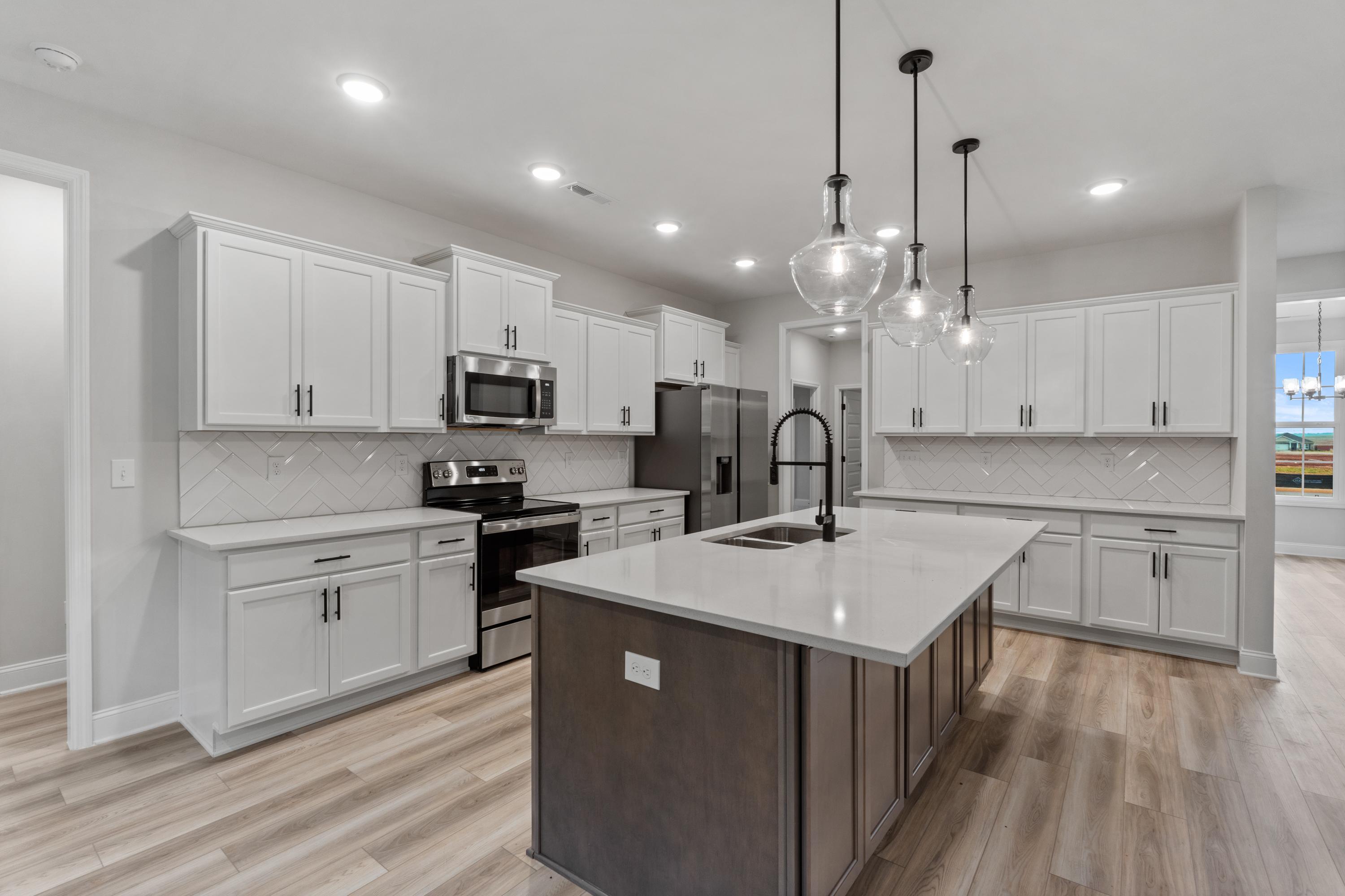 Spacious kitchen in The Oxford home design by Davidson Homes, featuring white shaker cabinets, quartz island with farmhouse sink, stainless appliances, subway tile backsplash