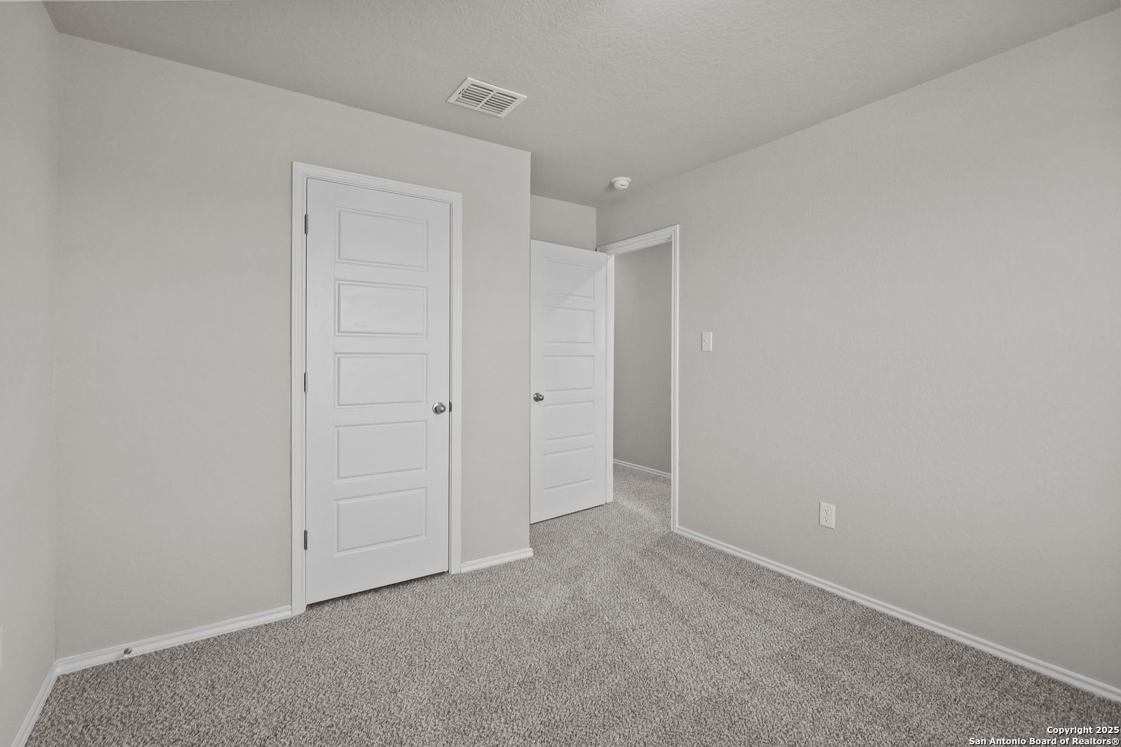 Spacious secondary bedroom with light gray walls, beige carpet, and double doors in Davidson Homes Trinity D, San Antonio