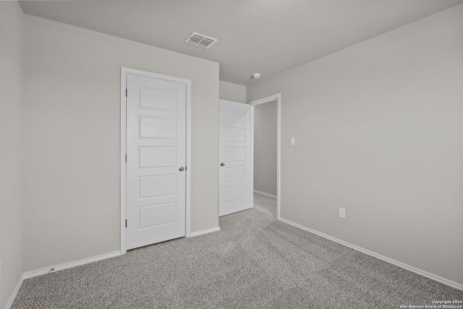 Spacious secondary bedroom with light gray walls, beige carpet, and double doors in Davidson Homes Trinity D, San Antonio
